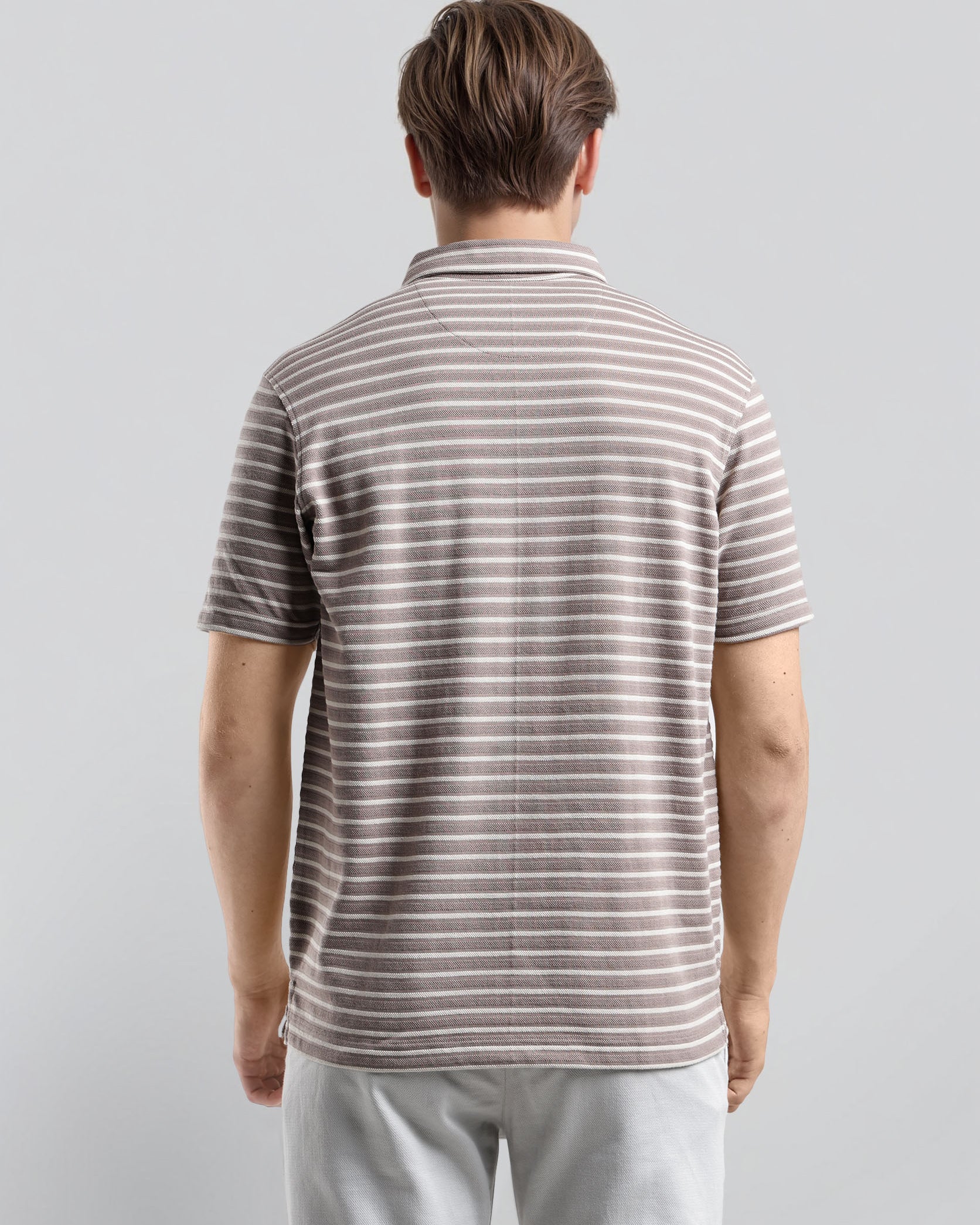 Man wearing a striped polo shirt and light pants against a plain background