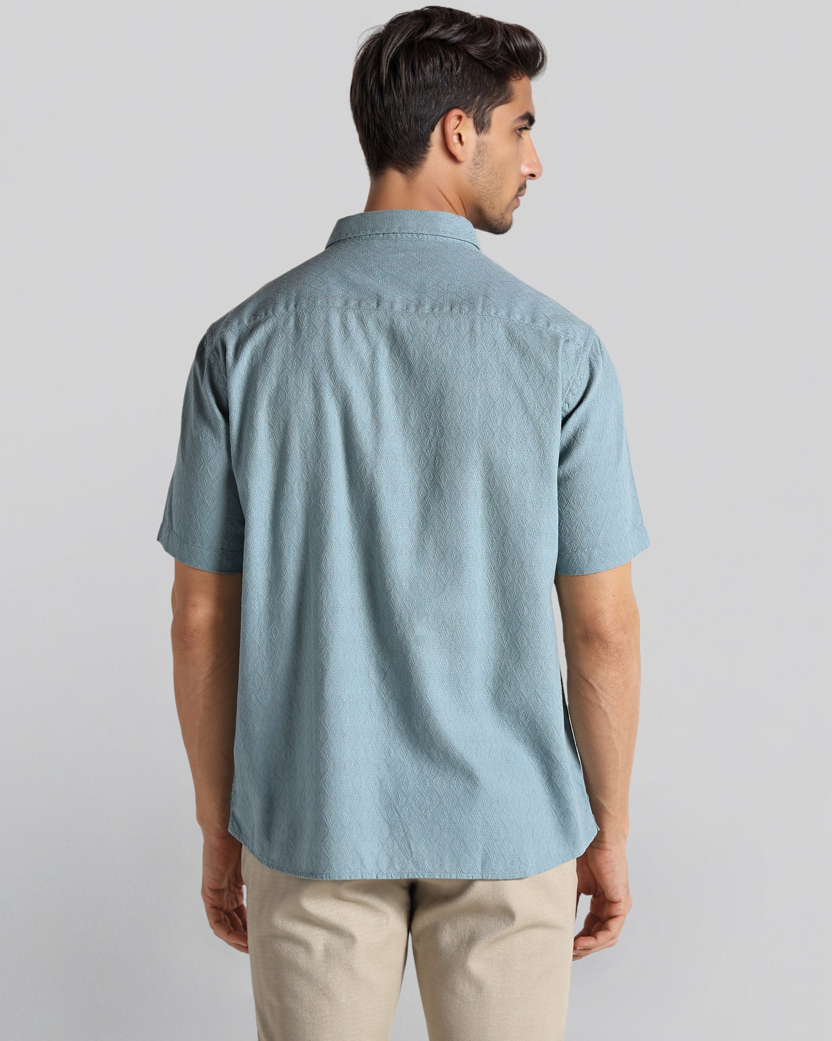 Man wearing a light blue short-sleeve shirt and beige pants on a plain background