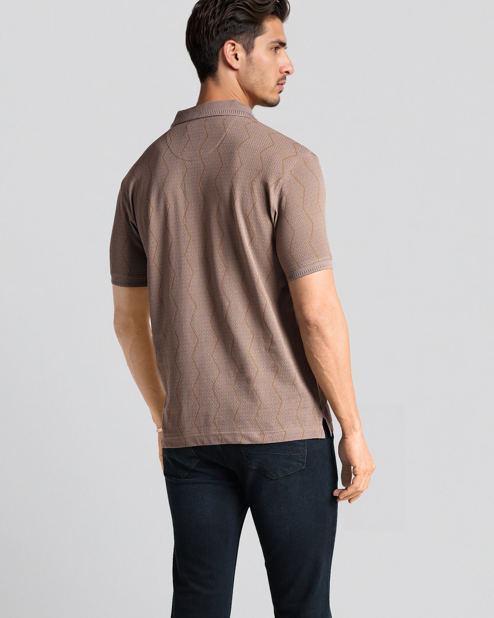 Man wearing a brown polo shirt and dark pants on a light gray background