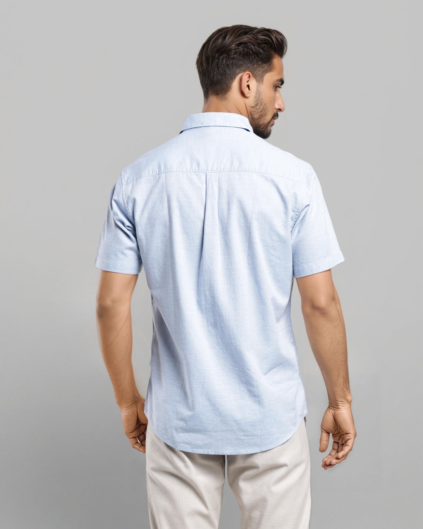 Man wearing a light blue polo shirt and beige pants on a gray background