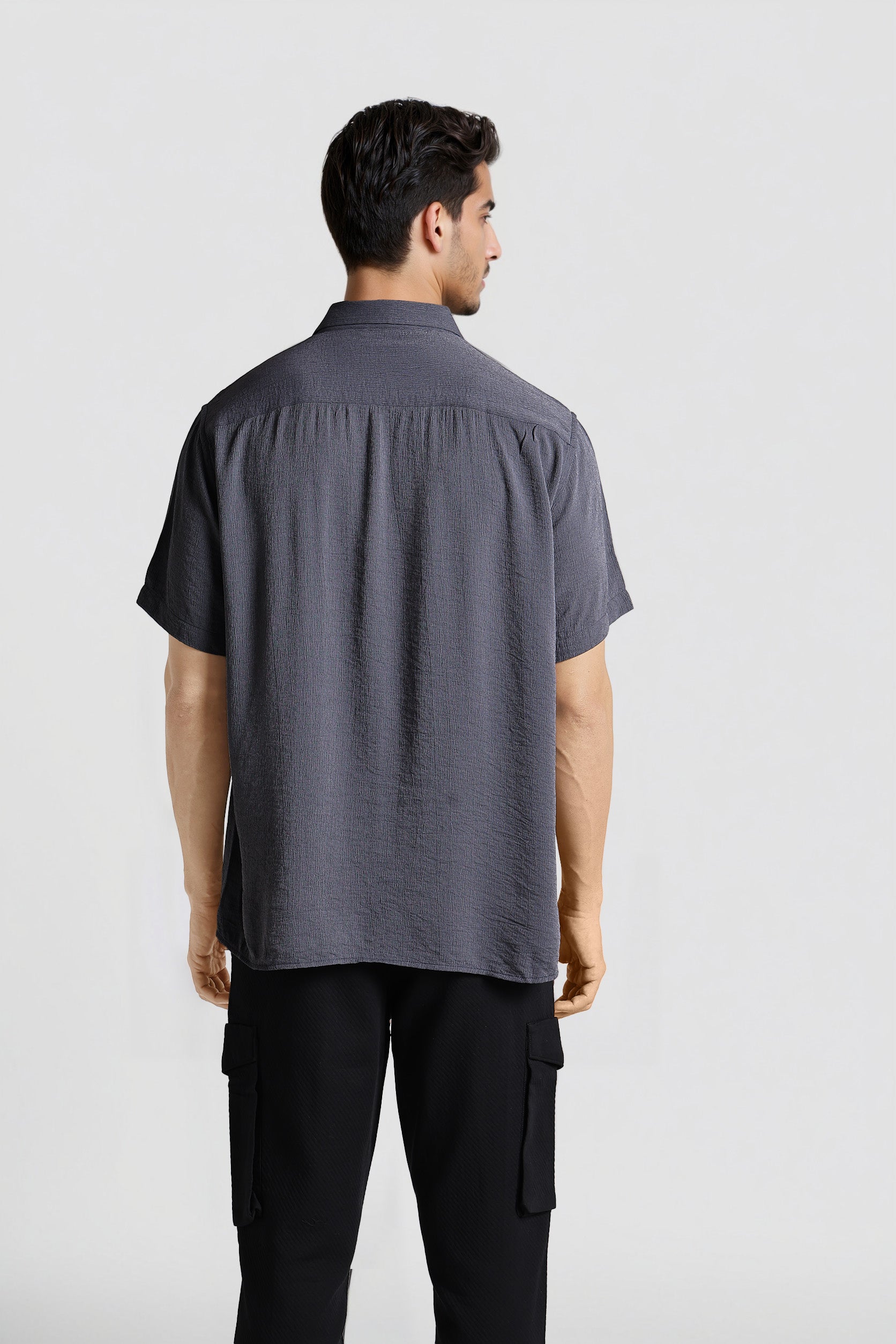 Man wearing a dark gray short-sleeve shirt and black pants on a light gray background