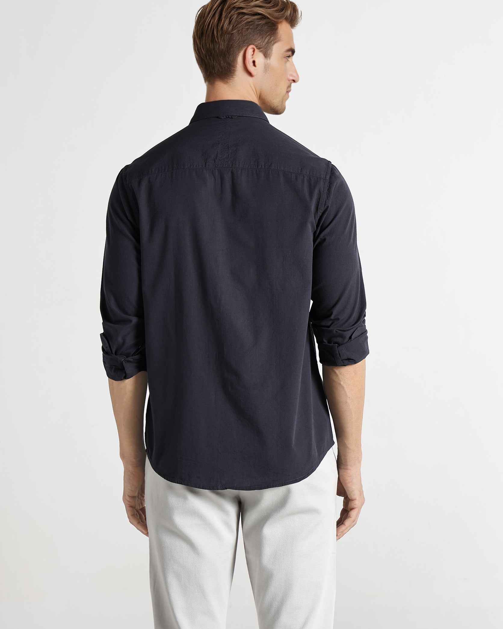 Man wearing a navy blue shirt and light gray pants on a white background