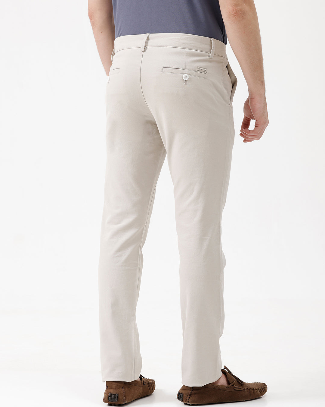 A person wearing light beige chino pants, a dark blue-gray t-shirt, and brown suede moccasin shoes, standing against a plain white studio background.