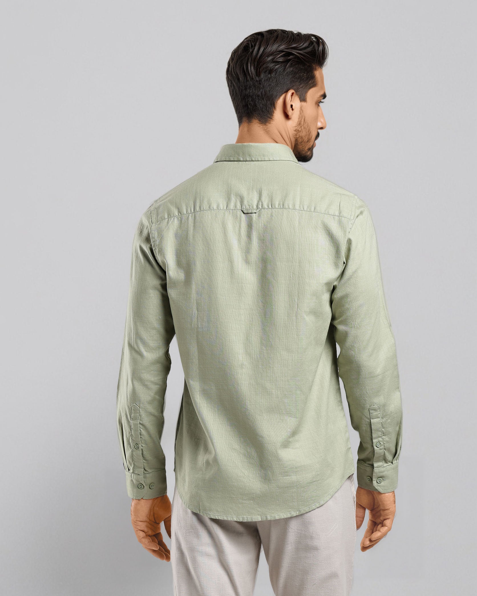 Man wearing a light green shirt and light gray pants on a plain background