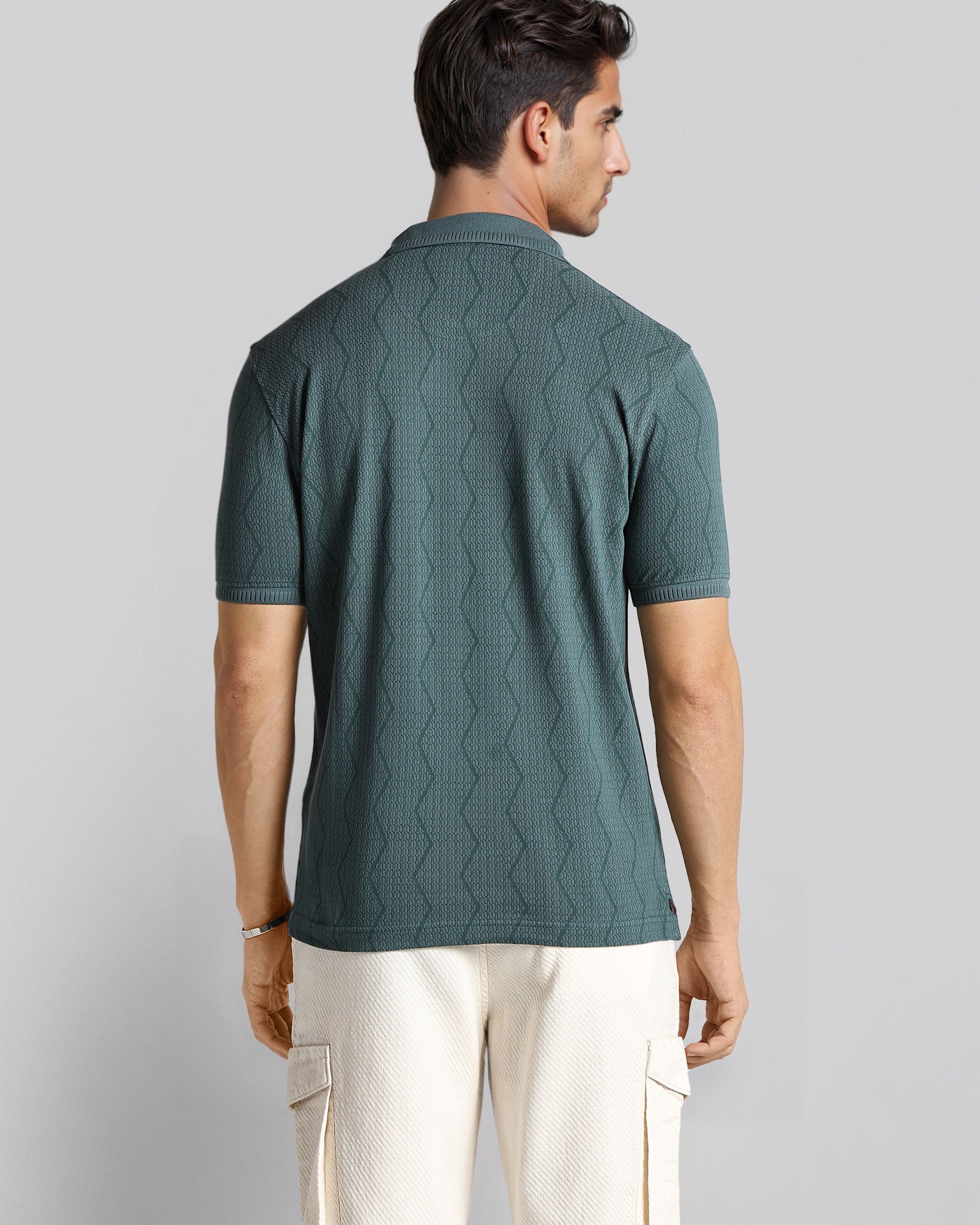 Man wearing a green textured polo shirt and white pants on a light gray background