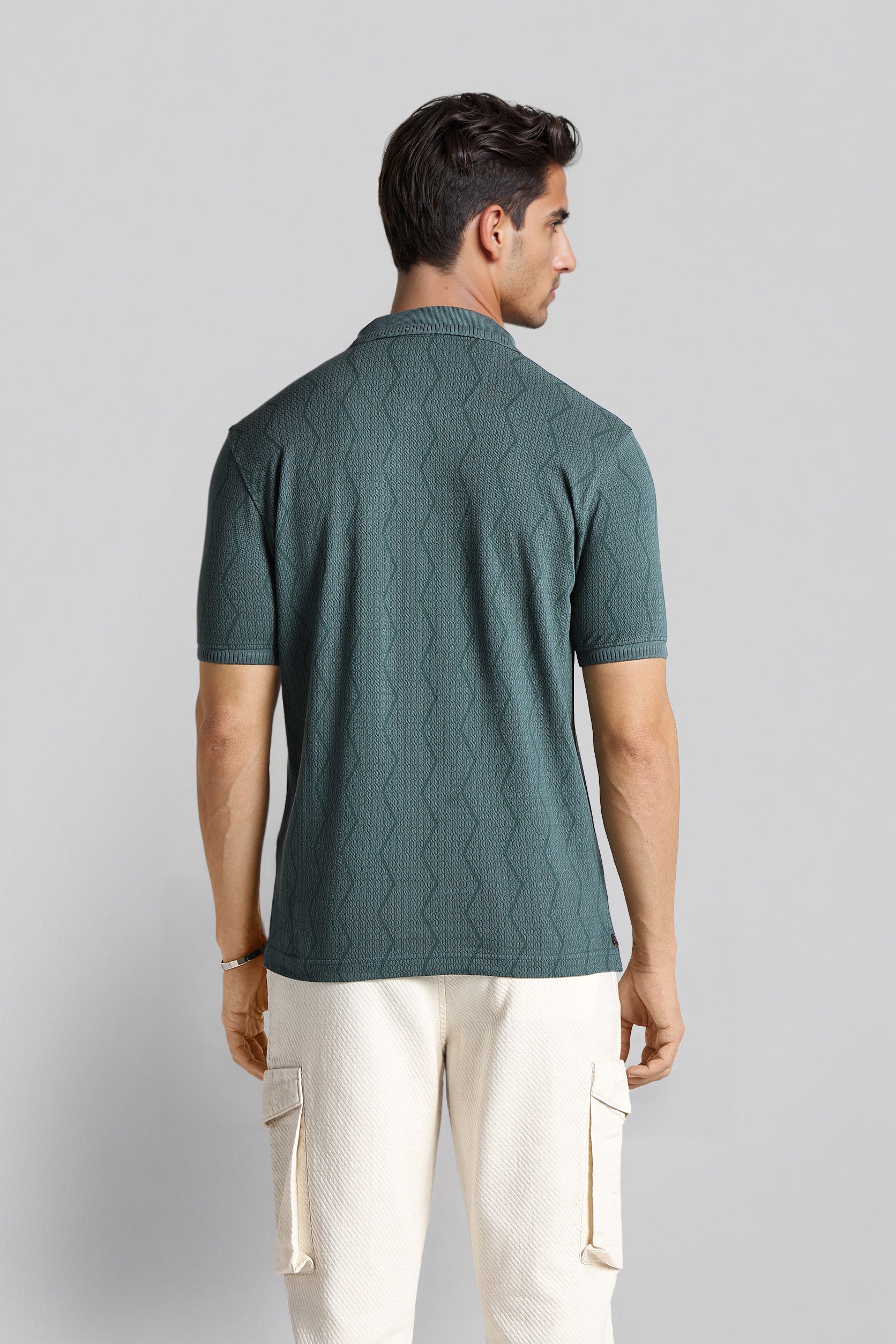 Man wearing a green textured polo shirt and white pants on a light gray background