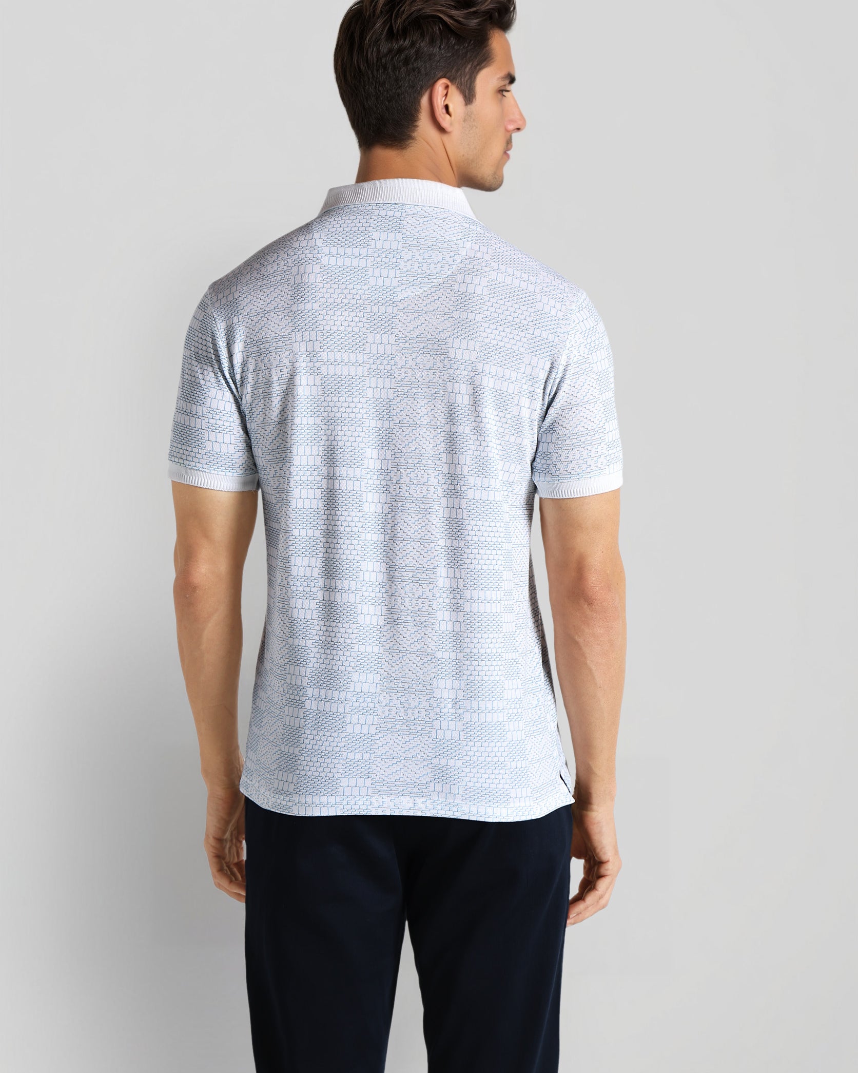 Man wearing a light gray patterned polo shirt and dark pants on a plain background