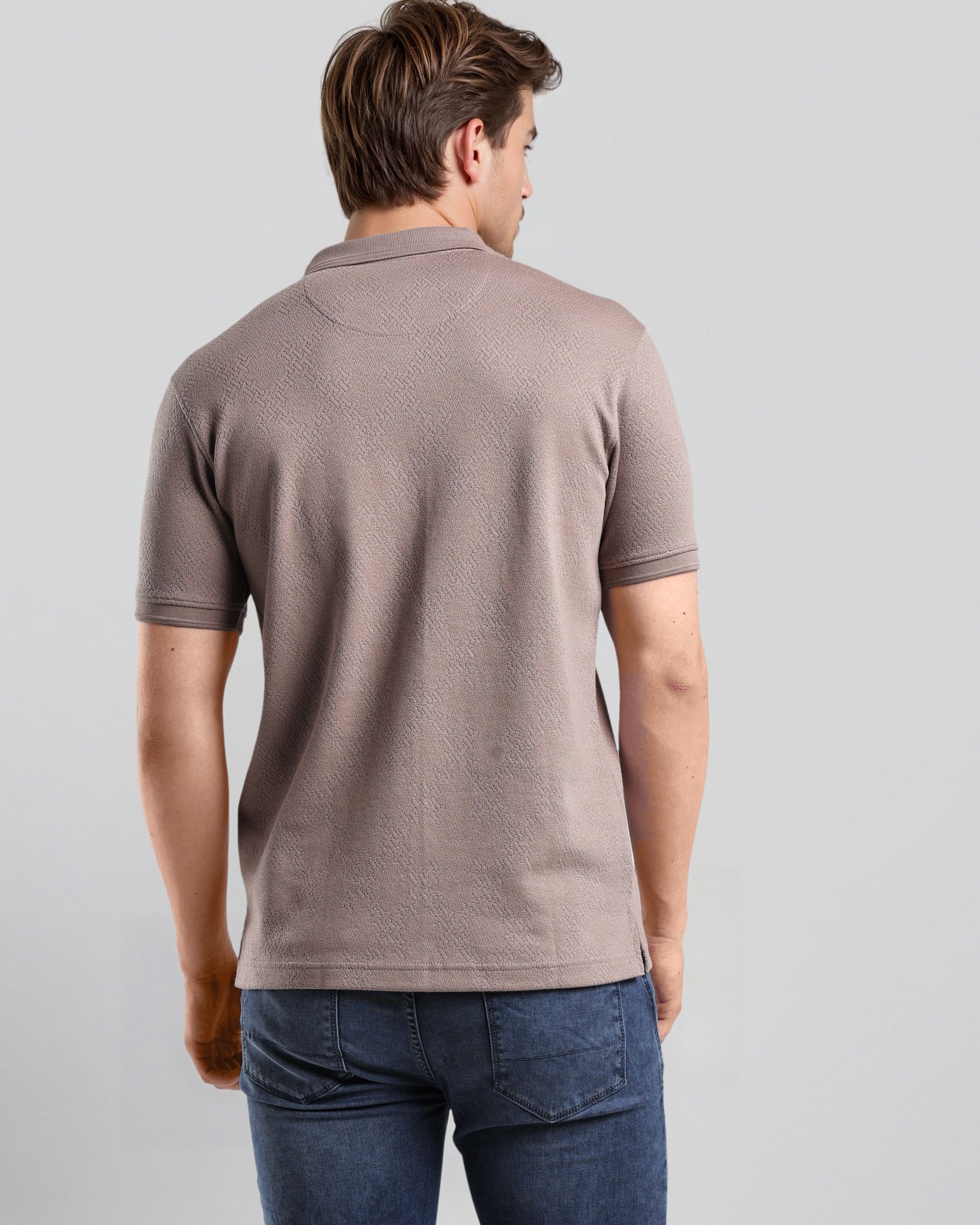 Man wearing a brown polo shirt and blue jeans on a light gray background