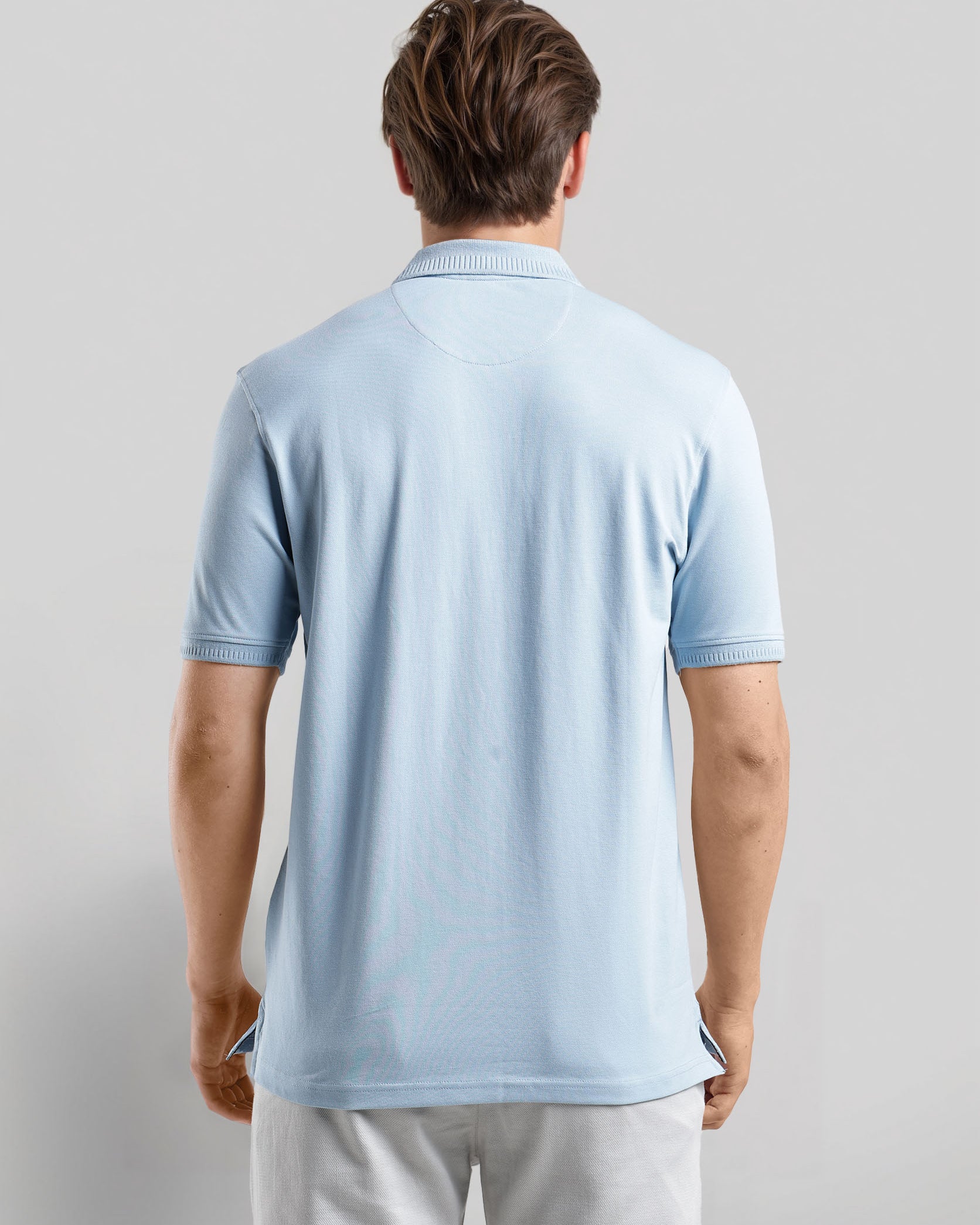 Man wearing a light blue polo shirt and light gray pants on a plain background