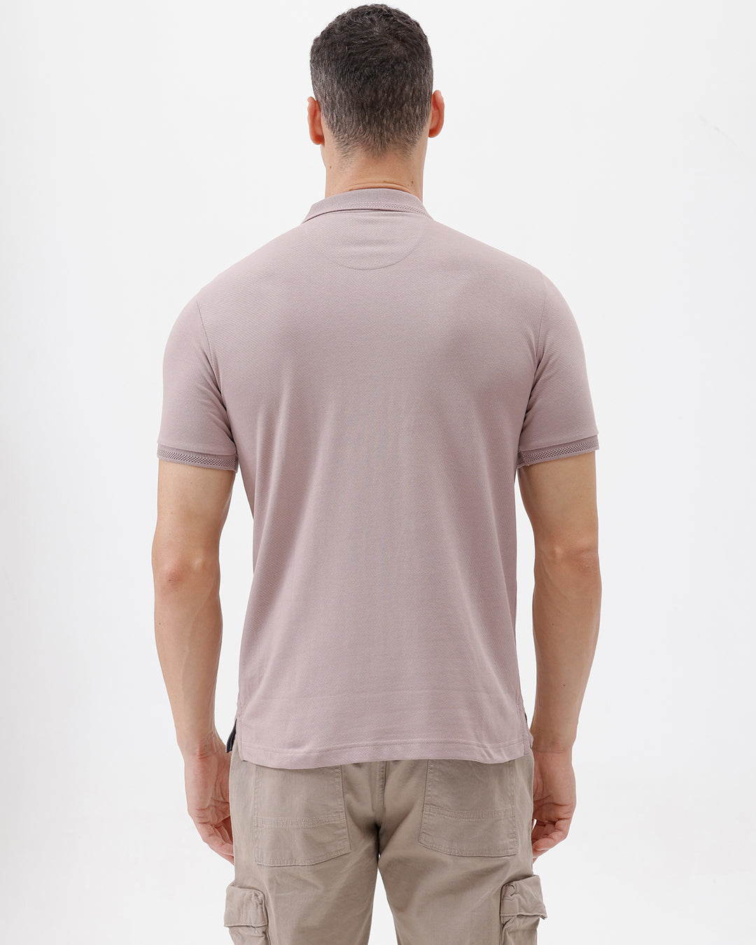 A man modeling a short-sleeve polo shirt in a dusty mauve-pink color, paired with khaki cargo pants and a baseball cap, against a plain light gray background.