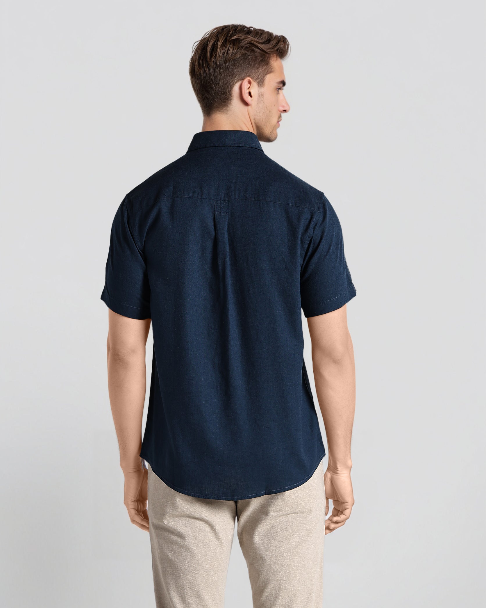 Man wearing a navy blue shirt and beige pants on a light gray background