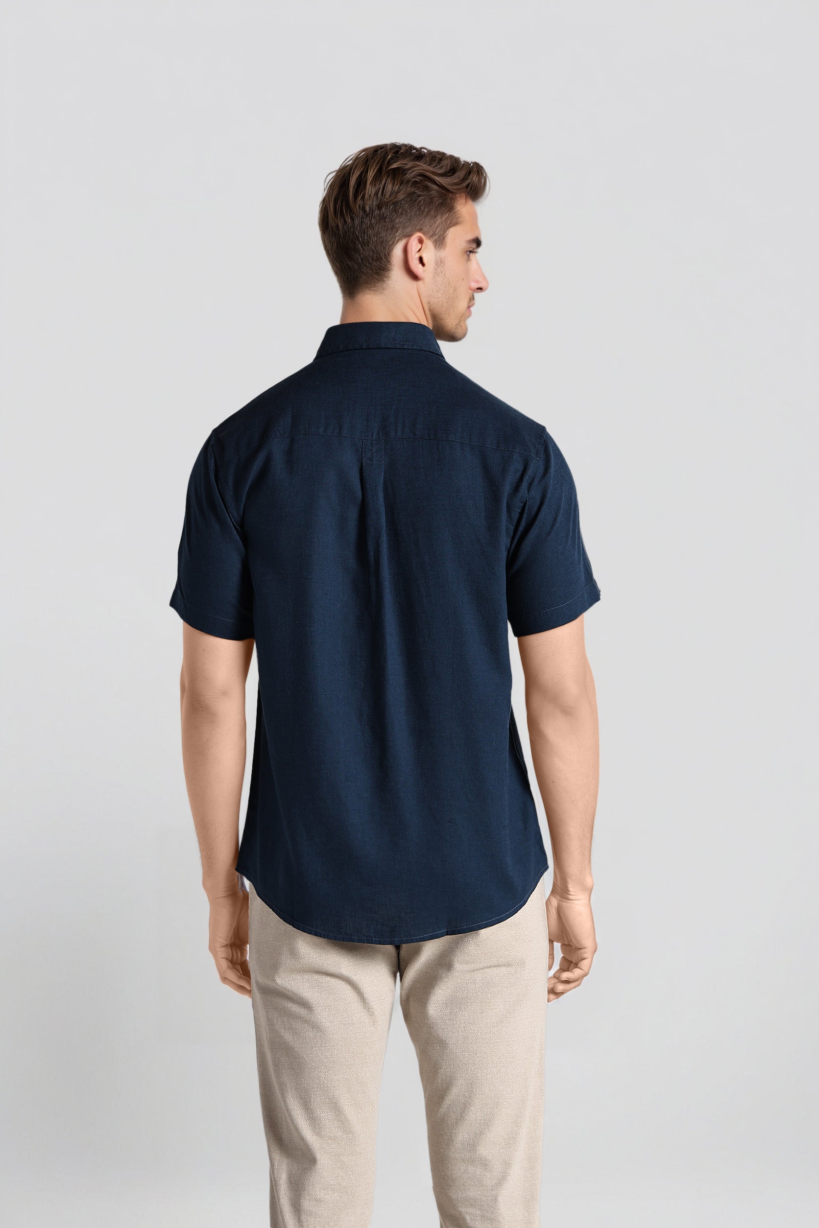 Man wearing a navy blue shirt and beige pants on a light gray background