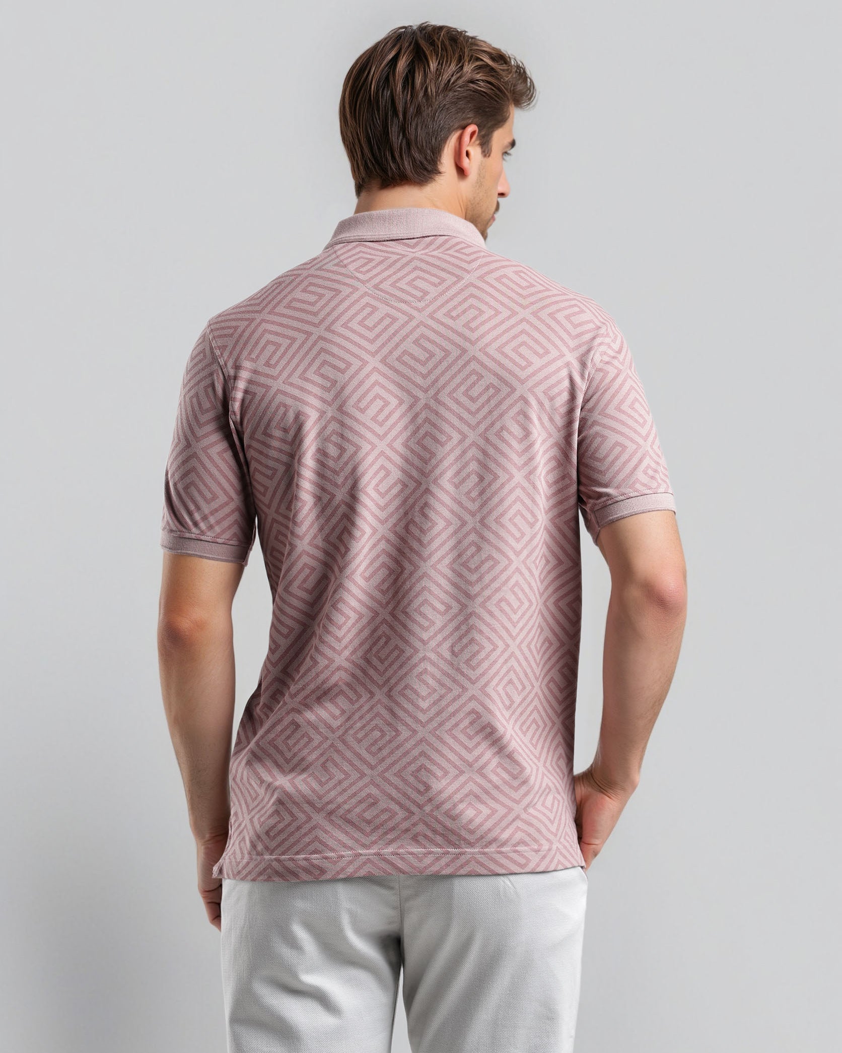 Man wearing a patterned pink polo shirt against a gray background