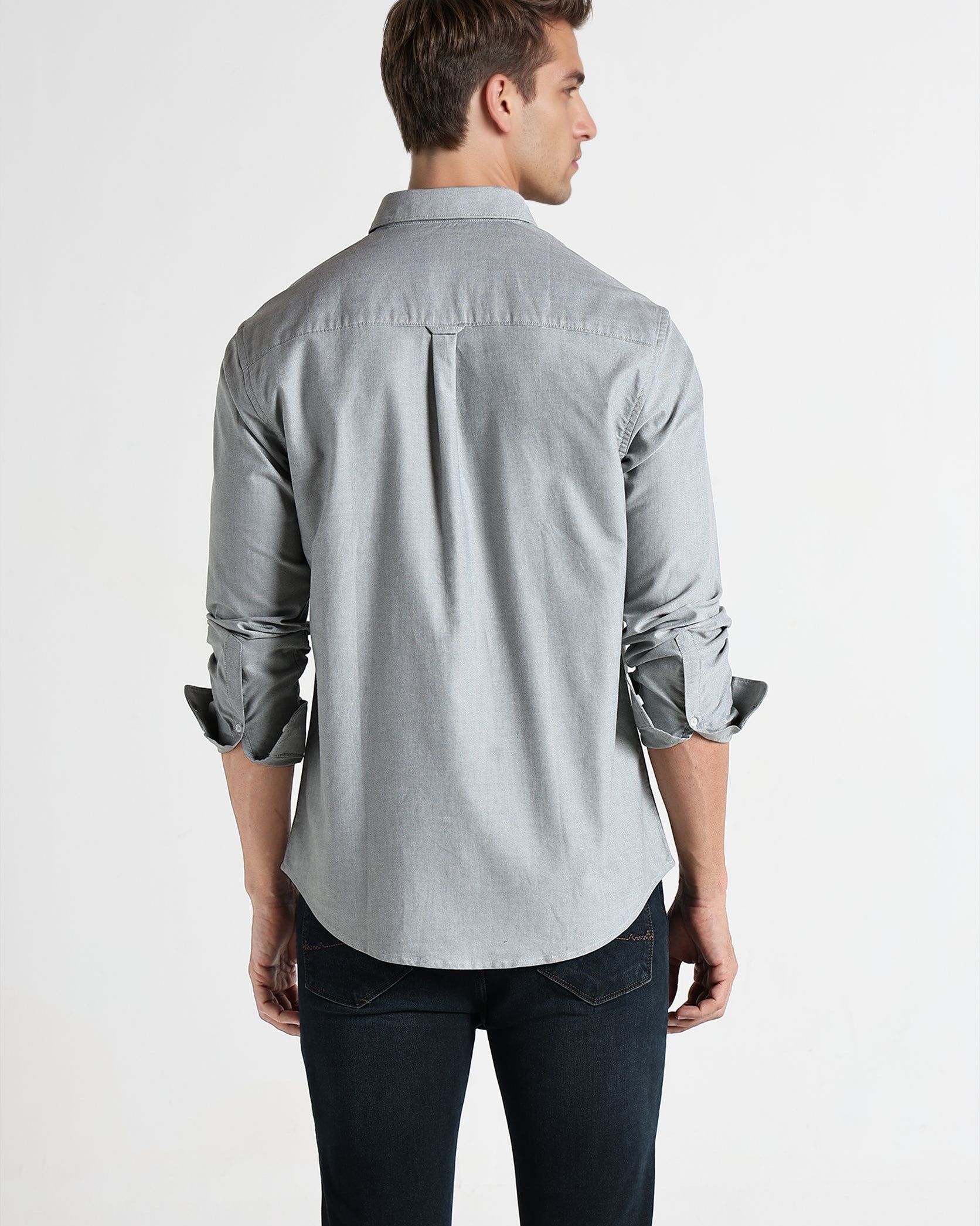 Man wearing a light gray button-up shirt and dark jeans on a white background