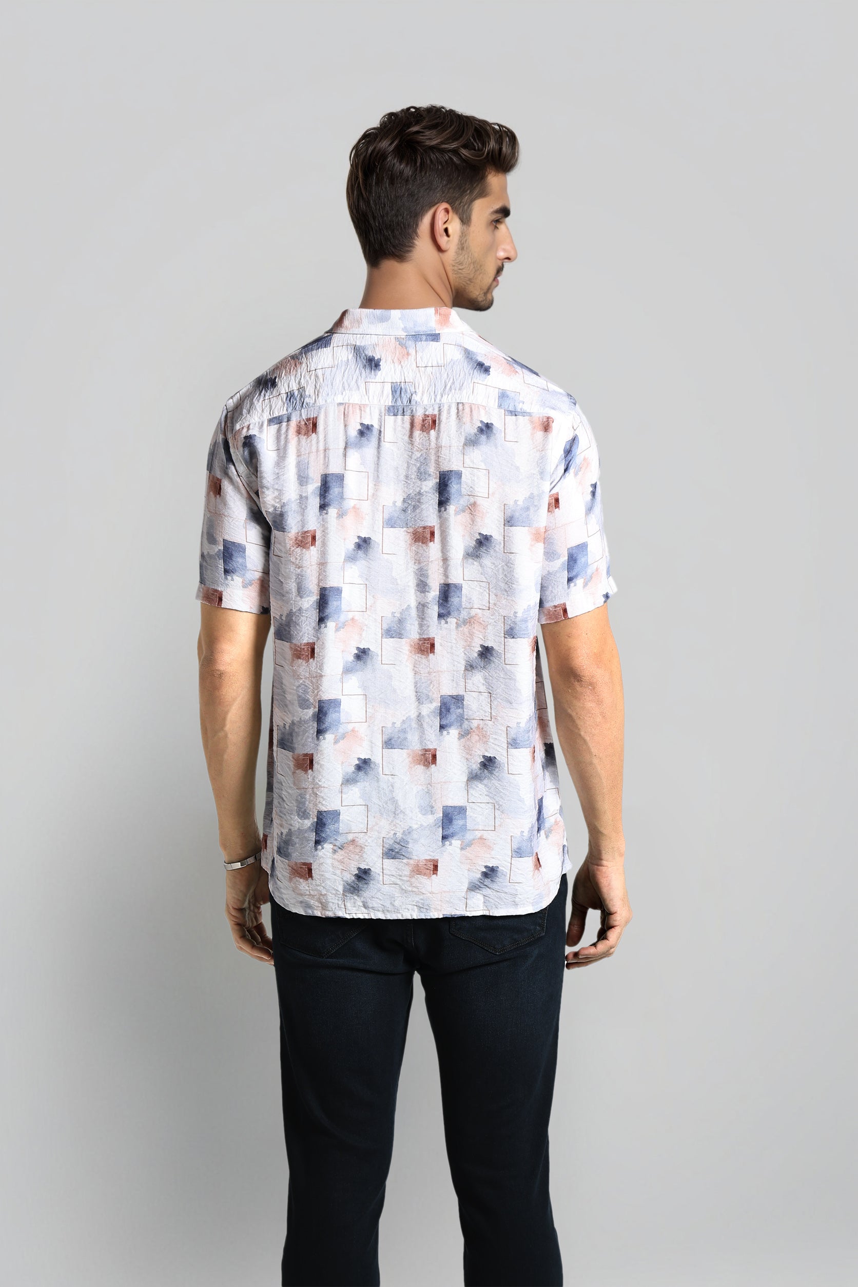 Man wearing a patterned shirt with short sleeves on a plain background