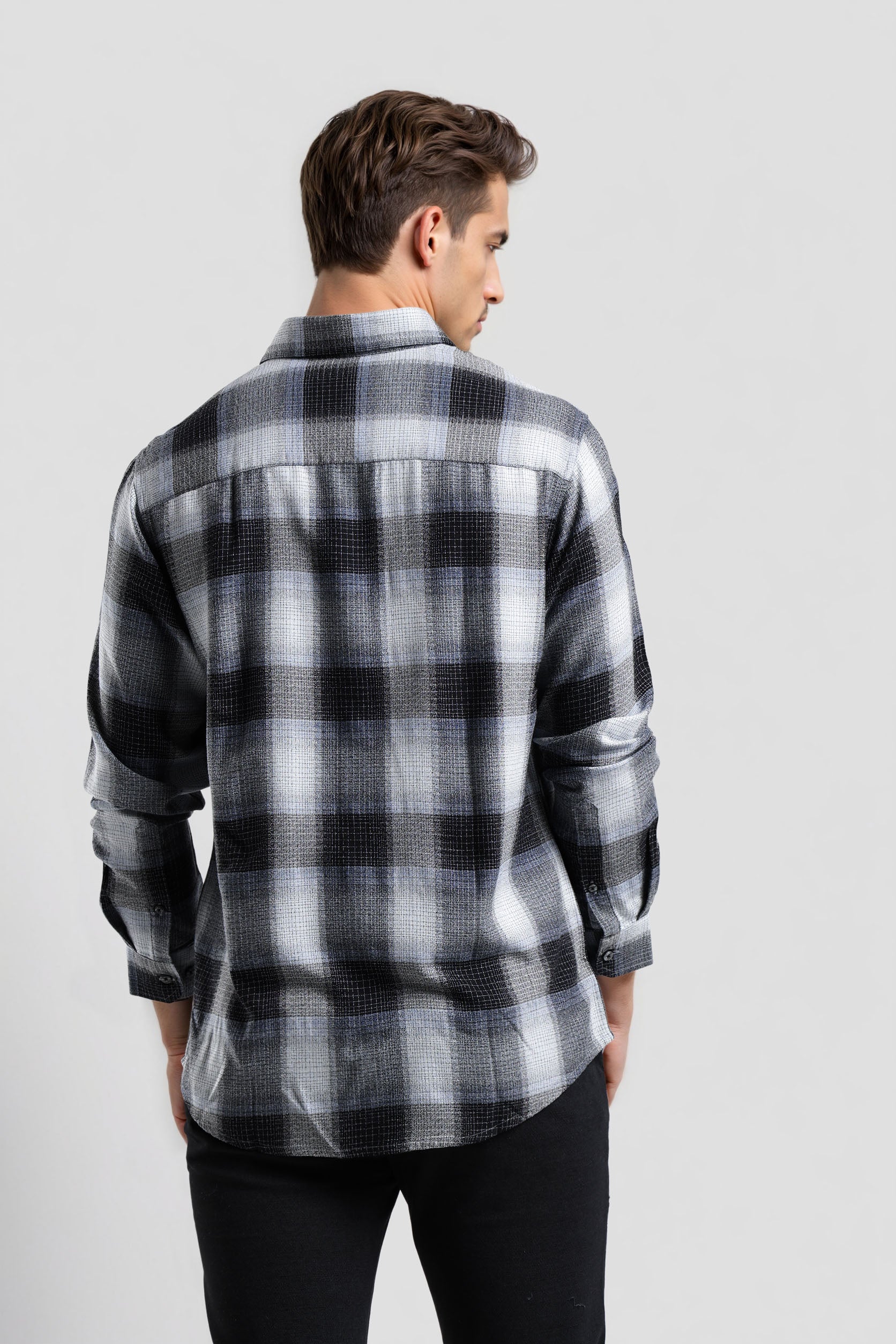 Man wearing a black and gray plaid shirt on a light gray background