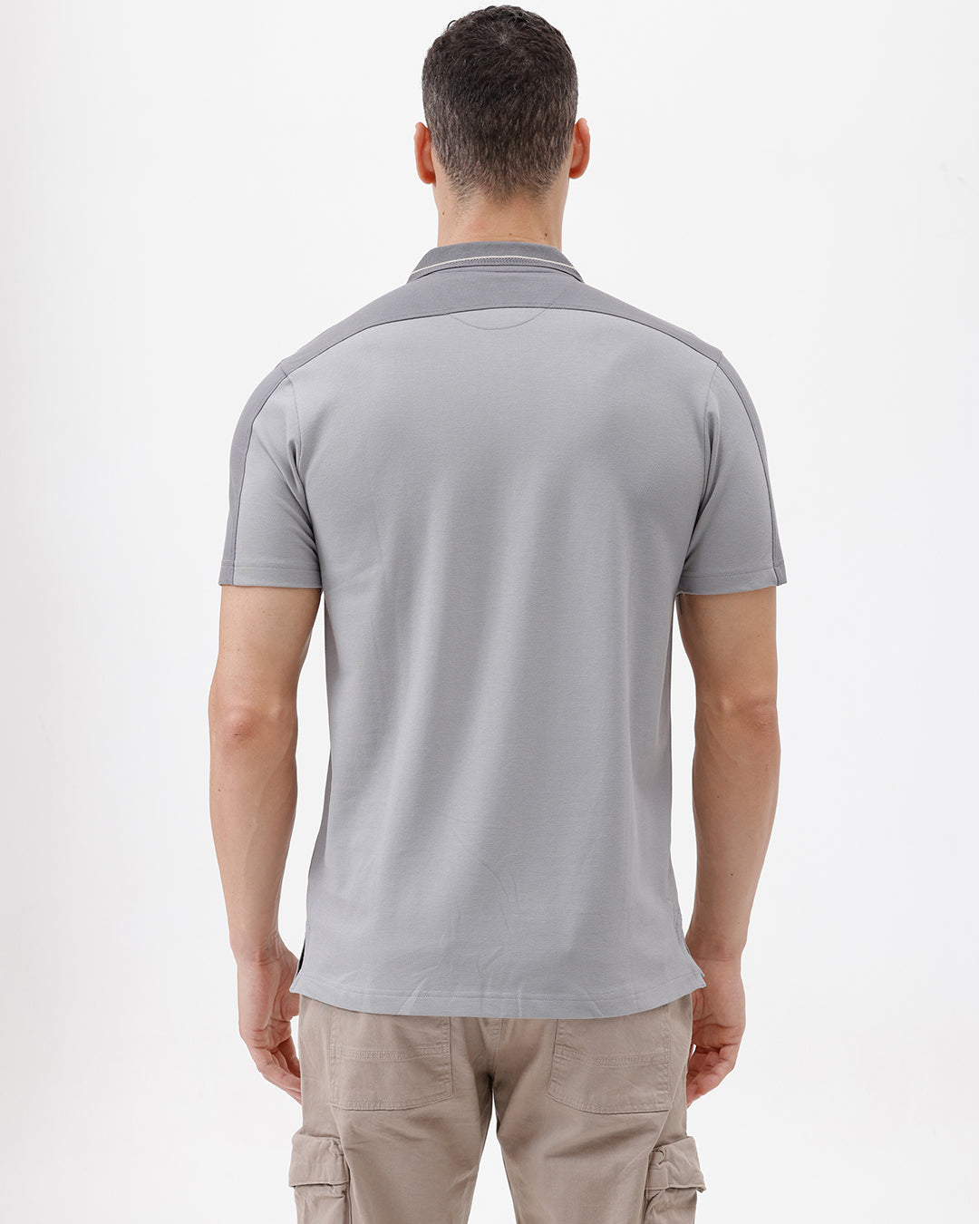 A man wearing a light gray short-sleeve polo shirt with darker gray shoulder panels and a small crest logo on the left chest, paired with khaki cargo pants, against a plain light gray studio background.
