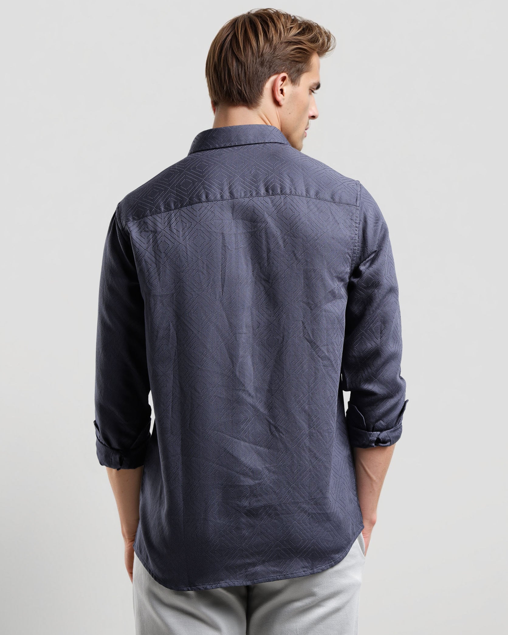 Man wearing a dark blue button-up shirt and light gray pants on a white background