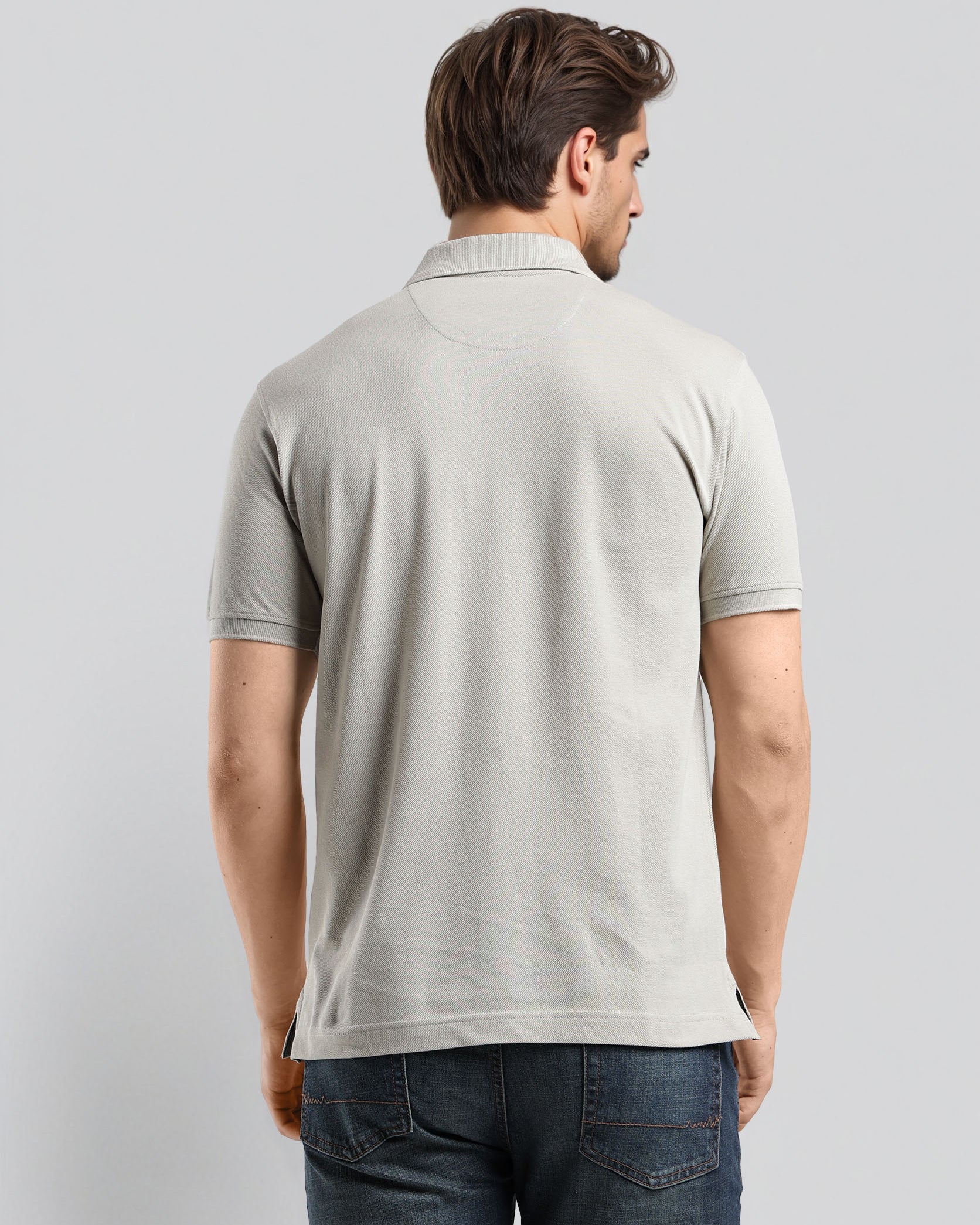 Man wearing a light gray polo shirt and blue jeans on a plain background