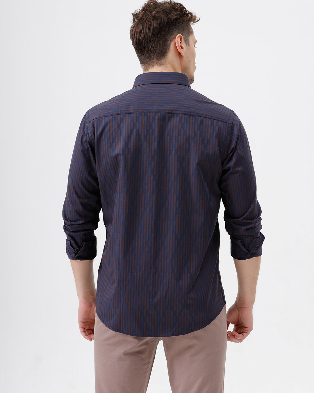 A man wearing a dark navy blue button-down shirt with thin vertical red stripes and light brown trousers, standing against a plain white studio background.