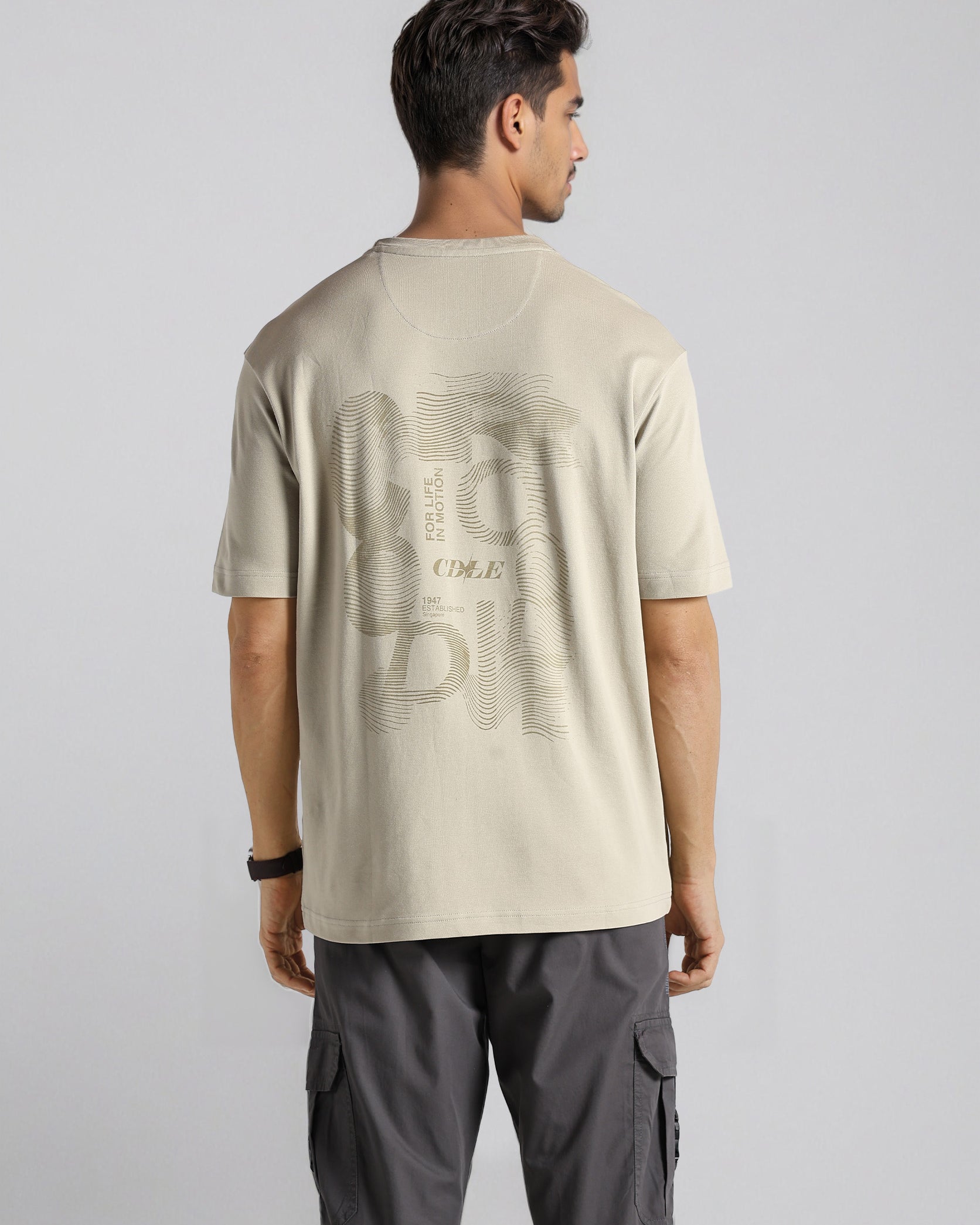 Man wearing a beige t-shirt with text on the back against a plain background