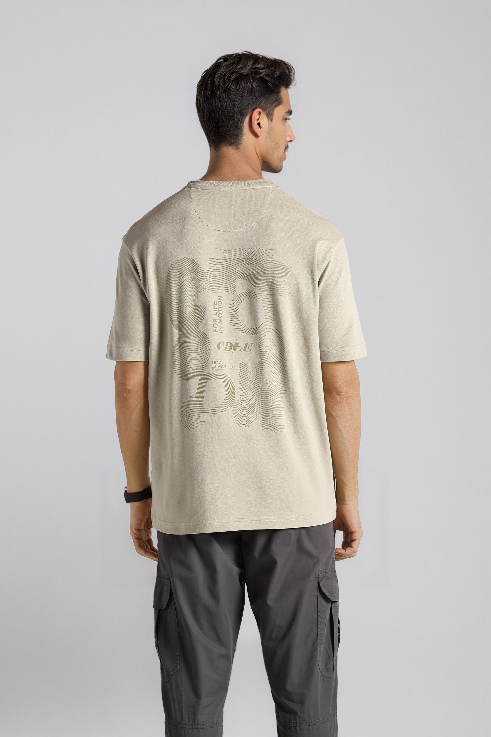Man wearing a beige t-shirt with text on the back against a plain background