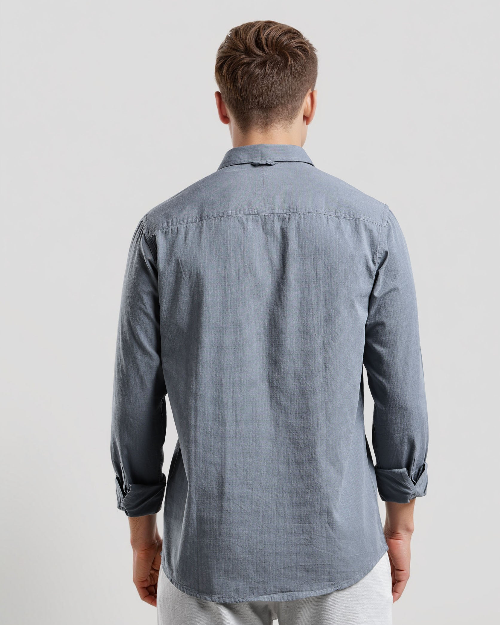 Man wearing a gray button-up shirt and white pants on a light gray background