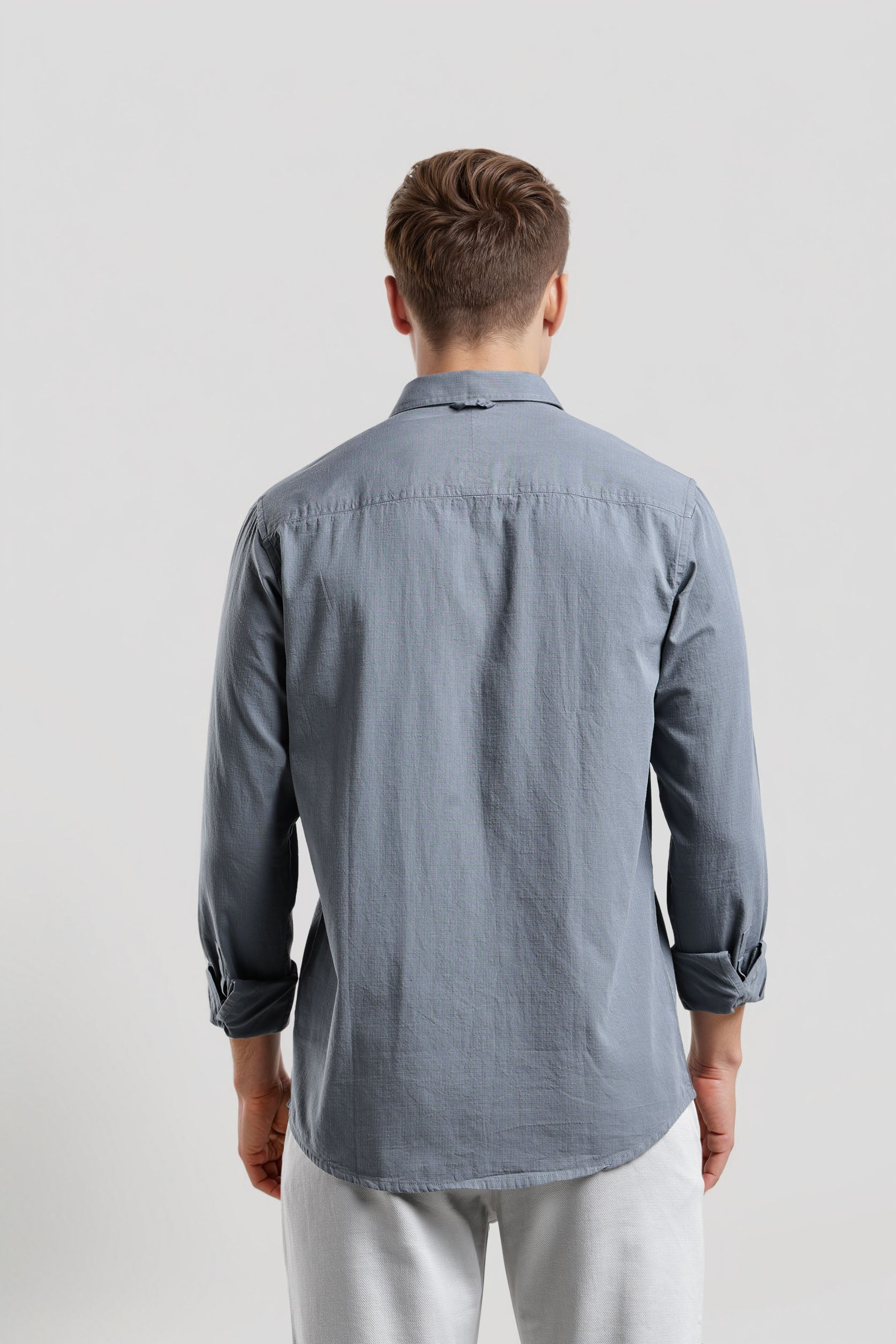 Man wearing a gray button-up shirt and white pants on a light gray background