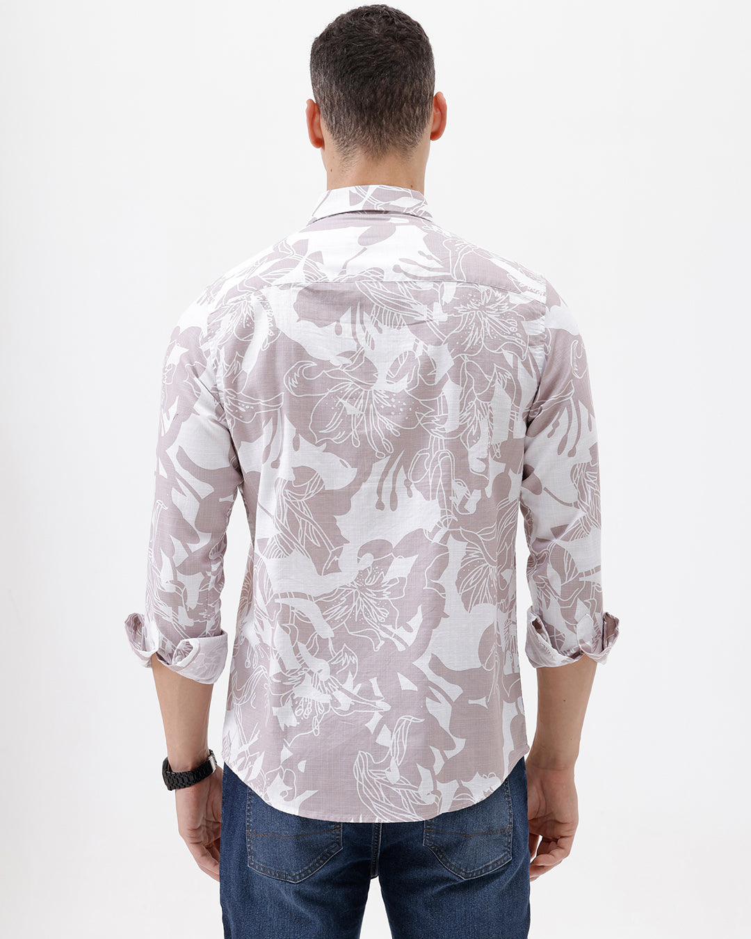 A man wearing a long-sleeve button-up shirt with a light gray and white abstract floral pattern, paired with dark blue jeans, standing against a plain white background.