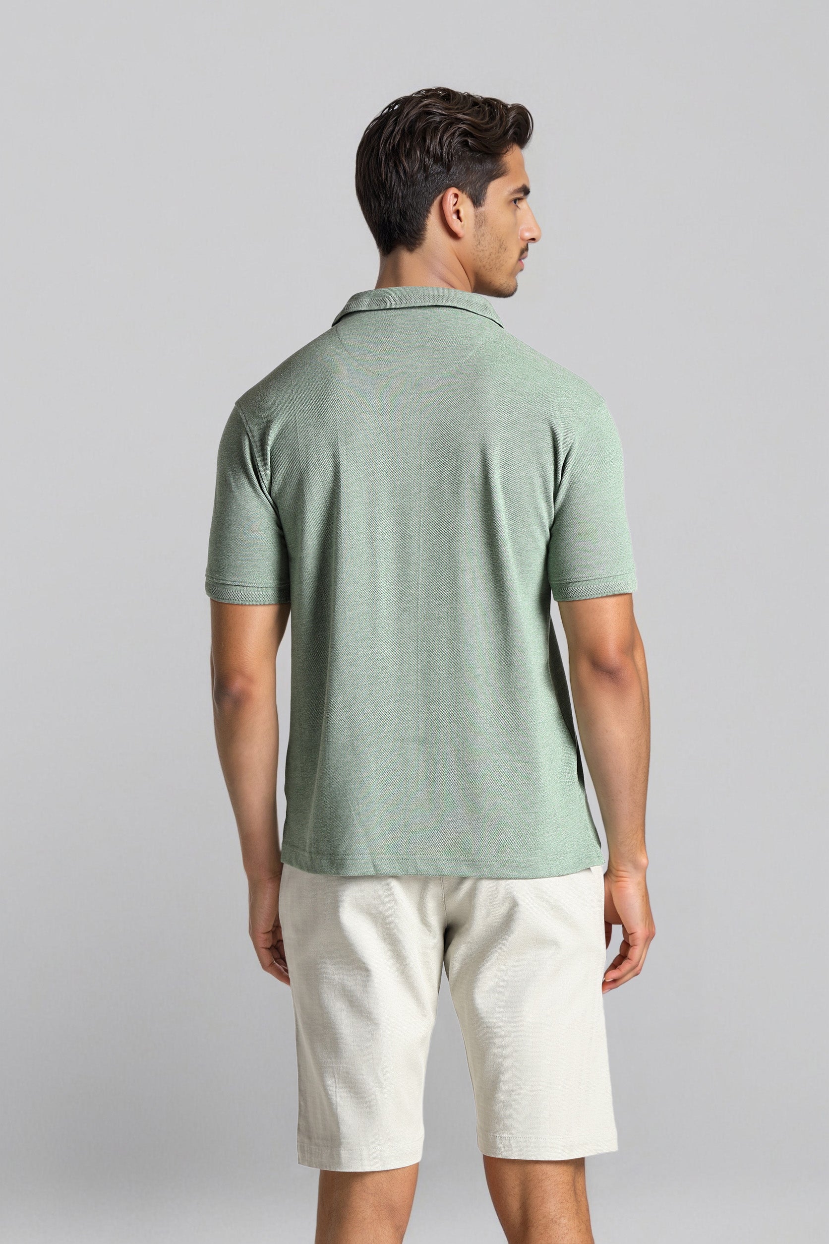 Man wearing a green polo shirt and white shorts on a gray background