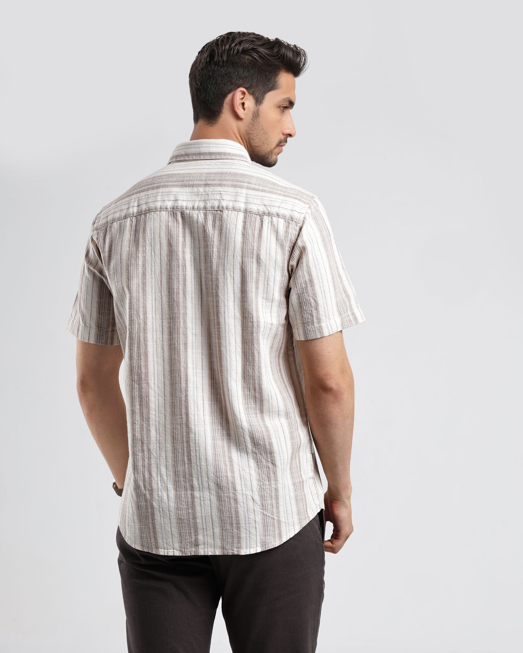 Man wearing a striped shirt and dark pants on a light gray background