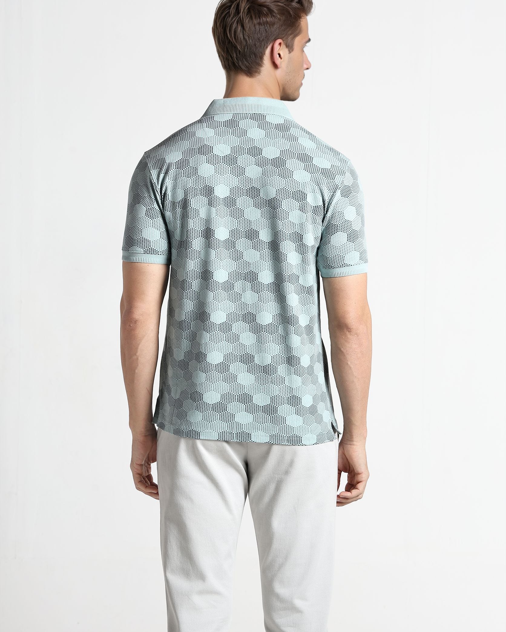 Man wearing a patterned polo shirt and light pants on a white background