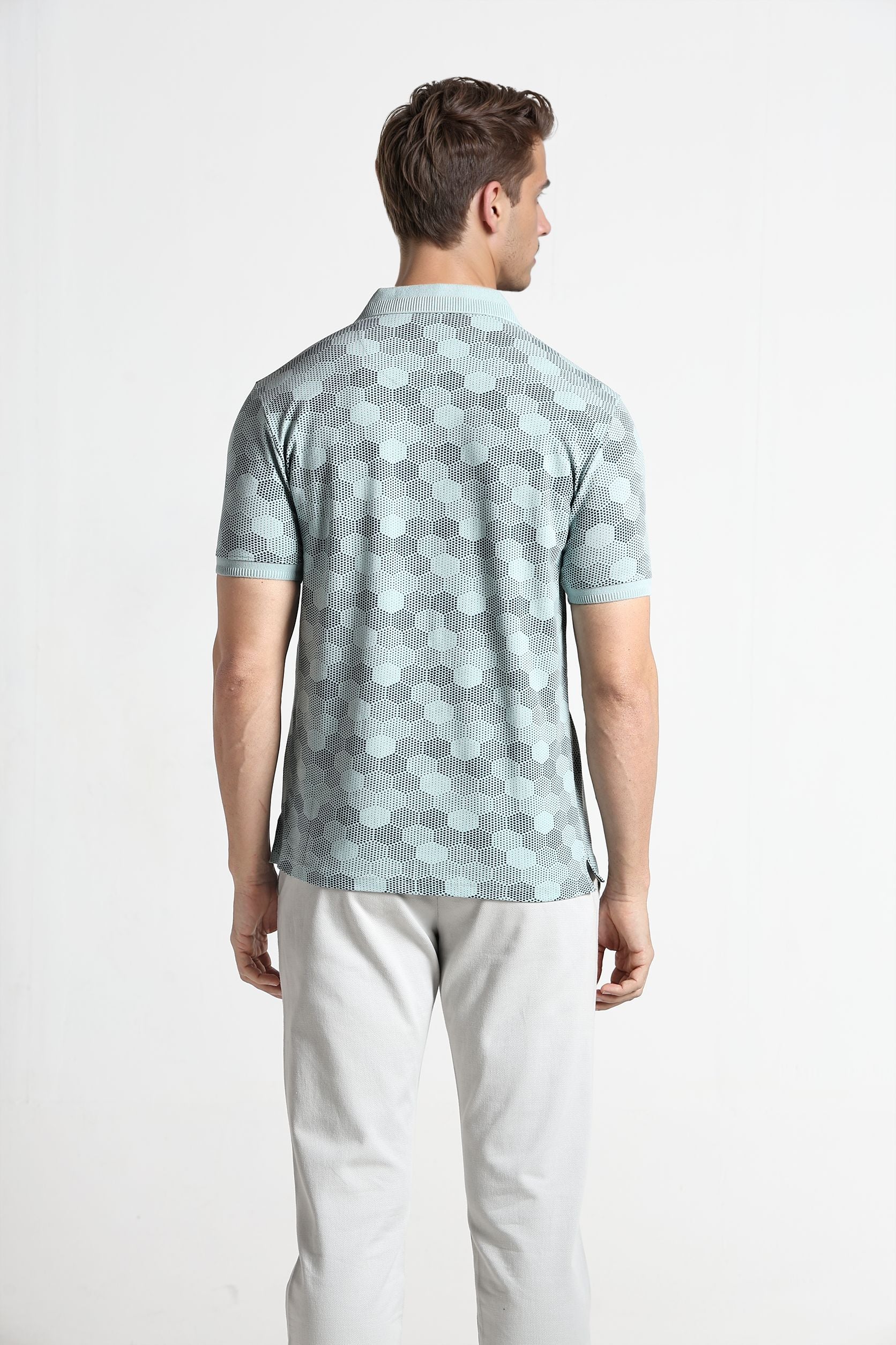 Man wearing a patterned polo shirt and light pants on a white background