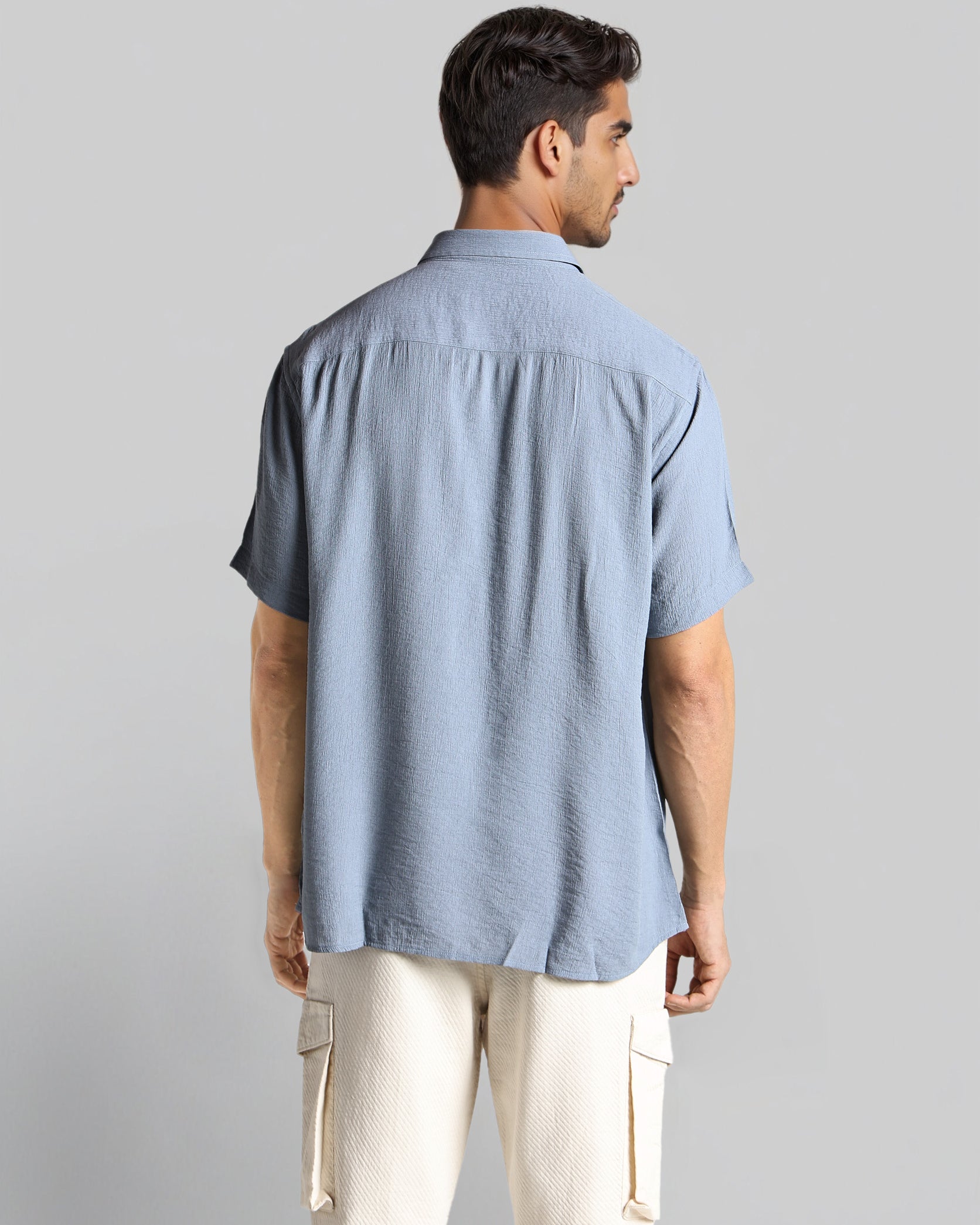 Man wearing a light blue shirt and beige pants against a gray background