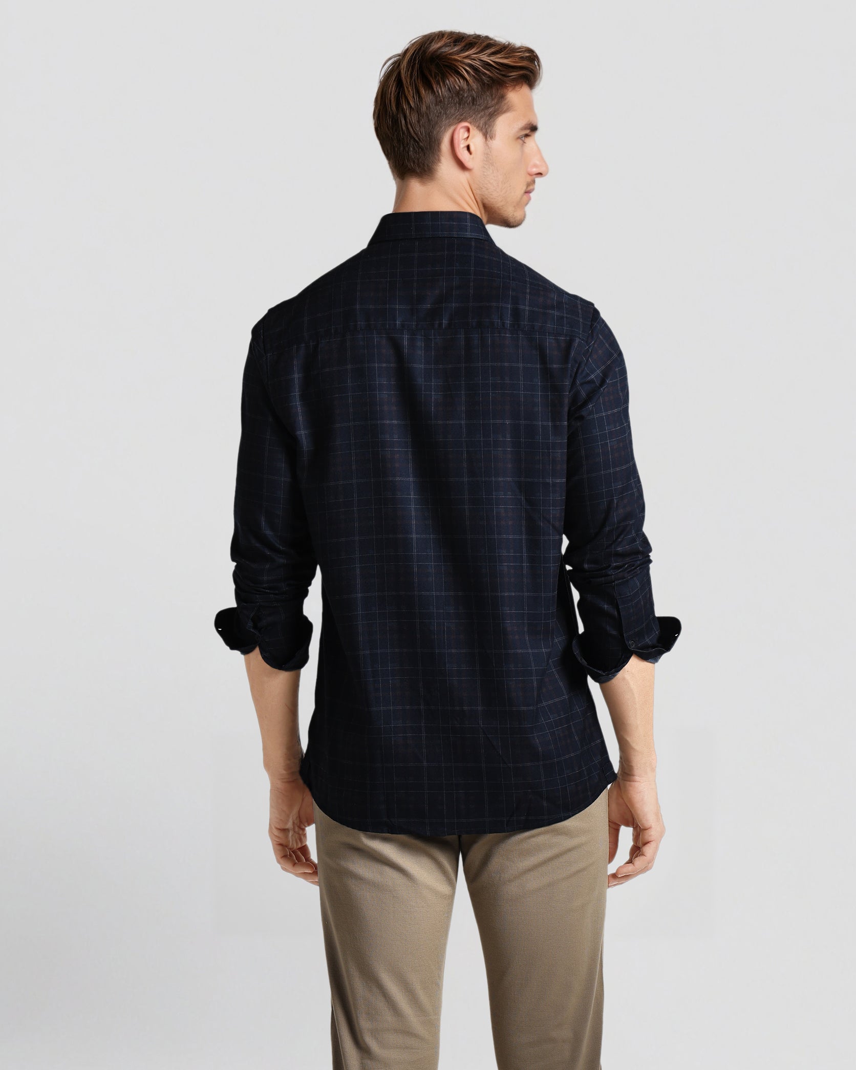 Man wearing a dark checkered shirt and beige pants on a light gray background