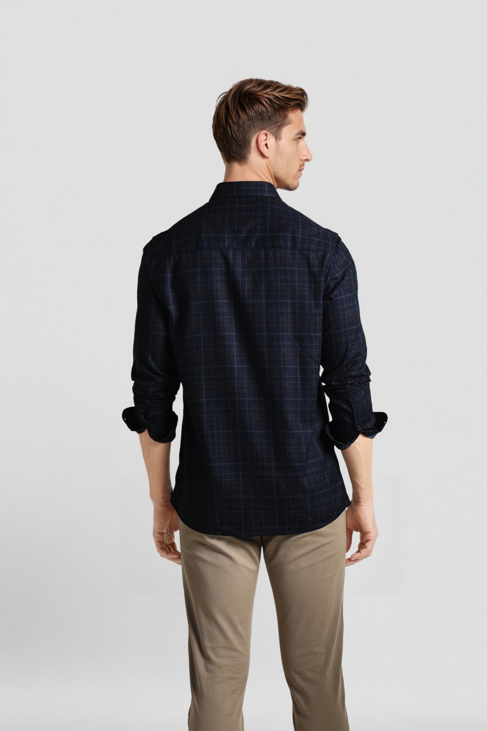 Man wearing a dark checkered shirt and beige pants on a light gray background