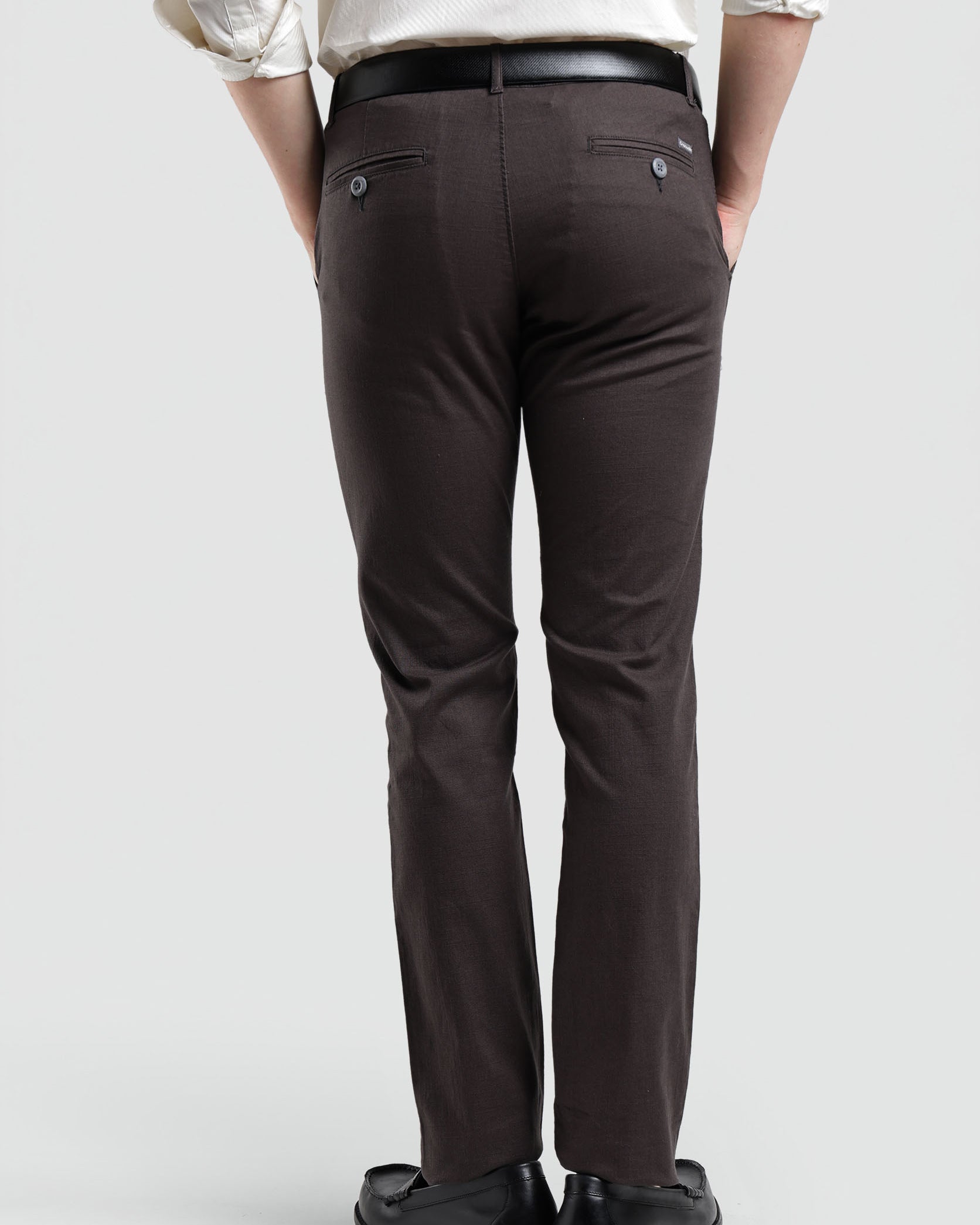 Person wearing brown pants and a white shirt on a plain background
