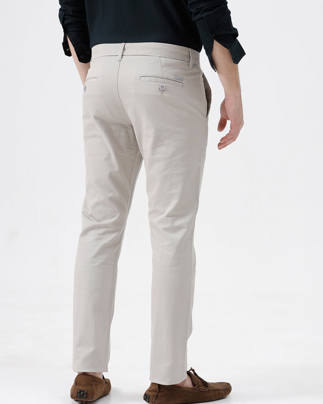 A person wearing slim-fit light beige chino pants, paired with a dark navy long-sleeve button-up shirt and brown suede moccasin-style shoes, photographed against a clean white studio background.