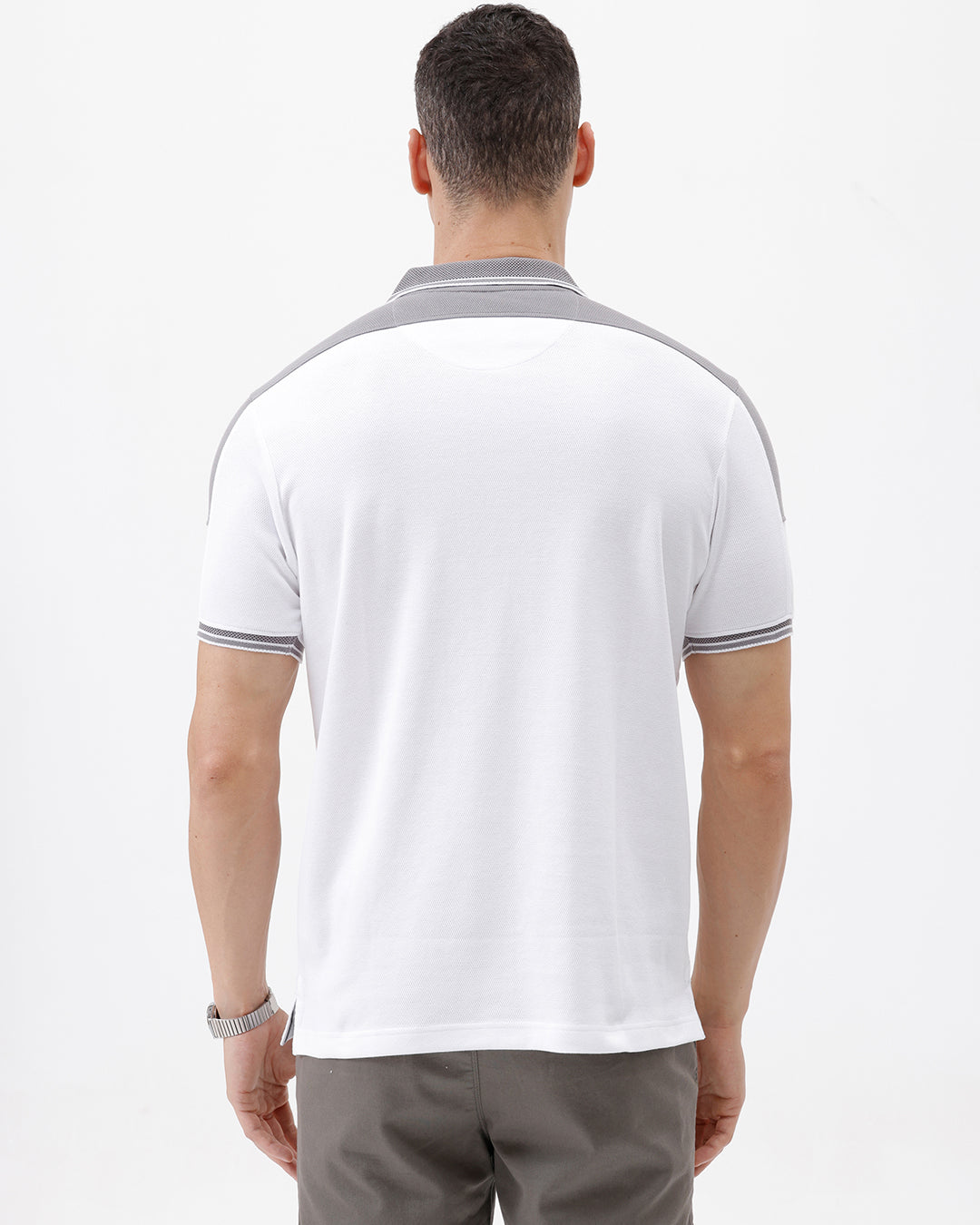 A man modeling a white short-sleeve polo shirt with gray shoulder panels and gray striped trim on the sleeves, paired with gray trousers and black sunglasses, against a plain white background.