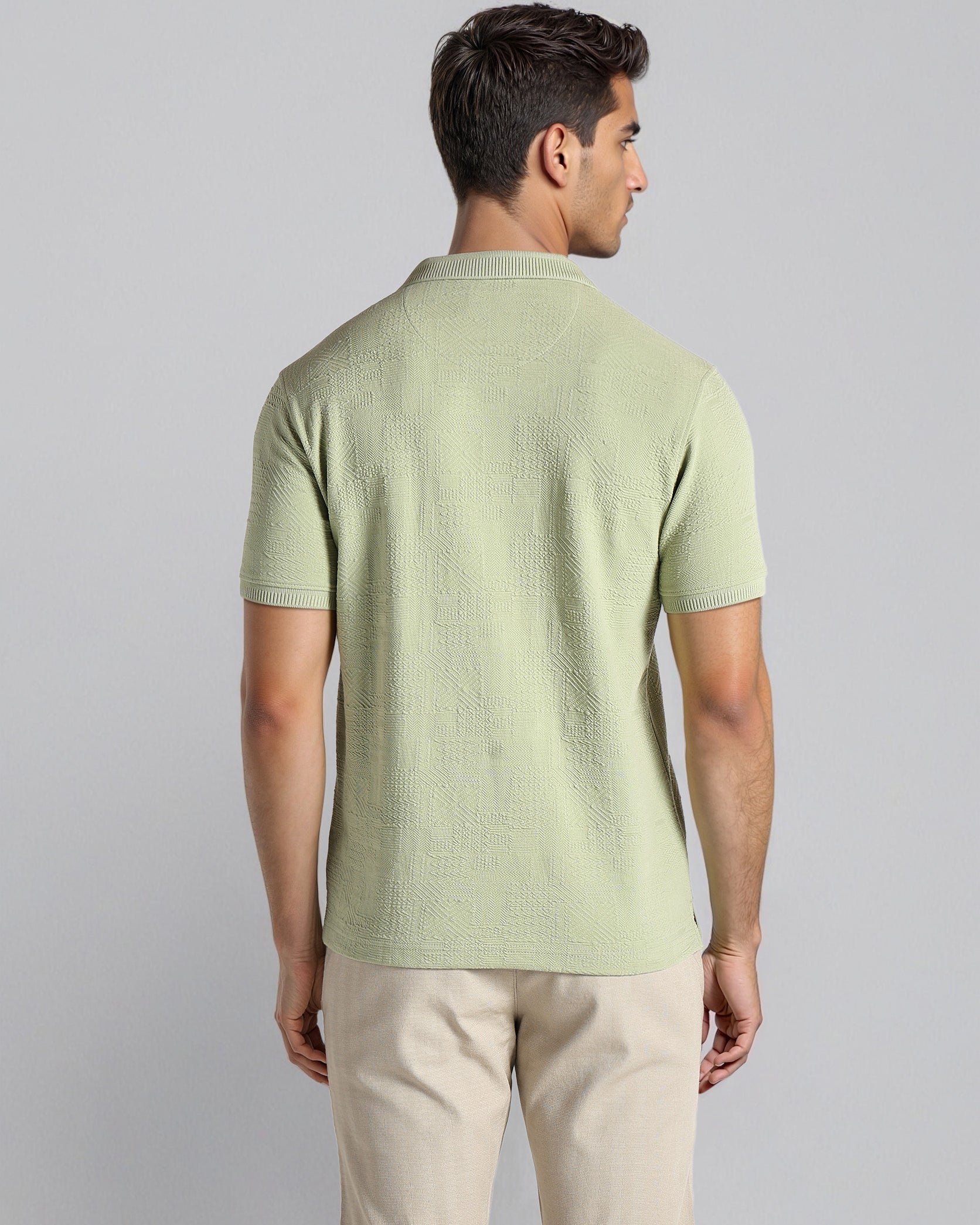 Man wearing a light green textured t-shirt and beige shorts on a gray background