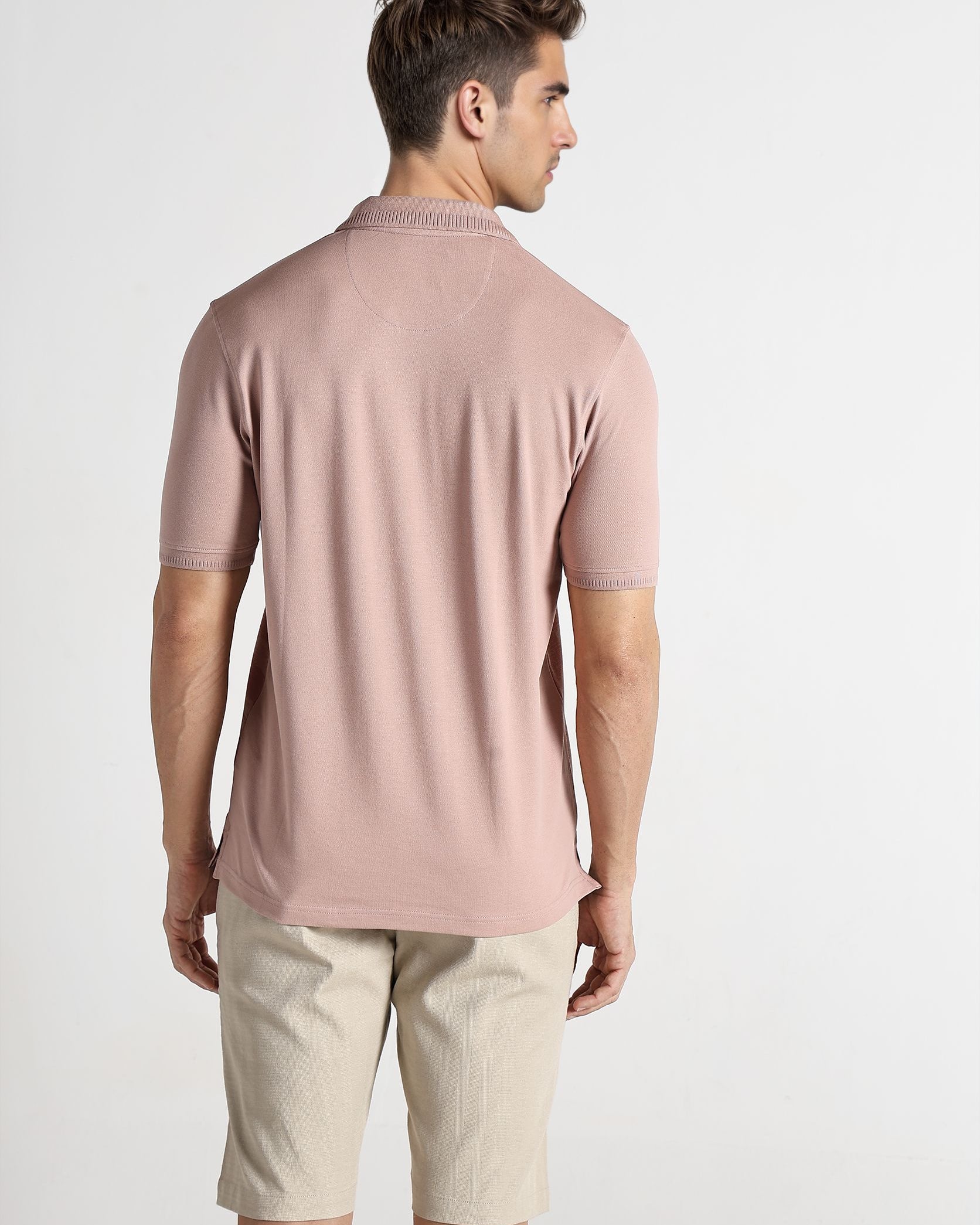 Man wearing a pink polo shirt and beige shorts on a white background