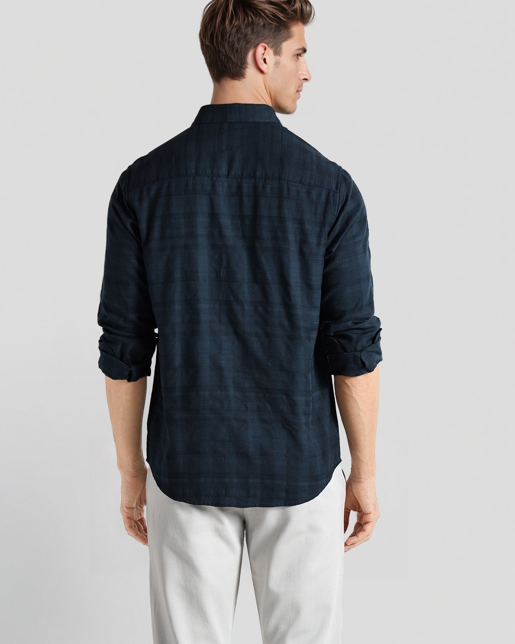 Man wearing a dark blue checkered shirt and light gray pants on a white background