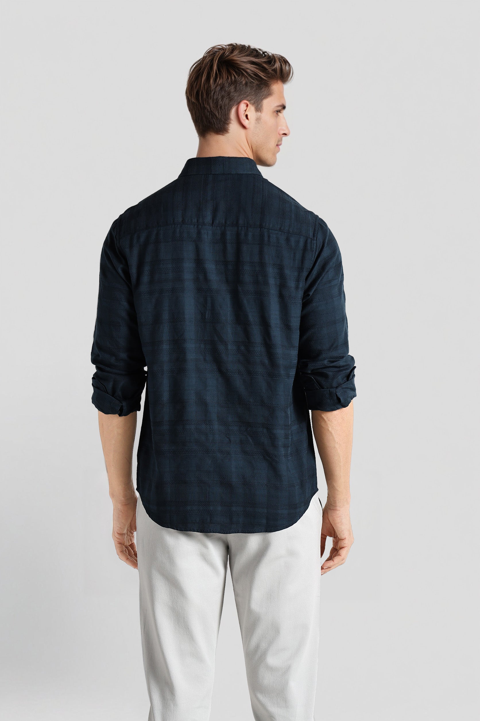 Man wearing a dark blue checkered shirt and light gray pants on a white background