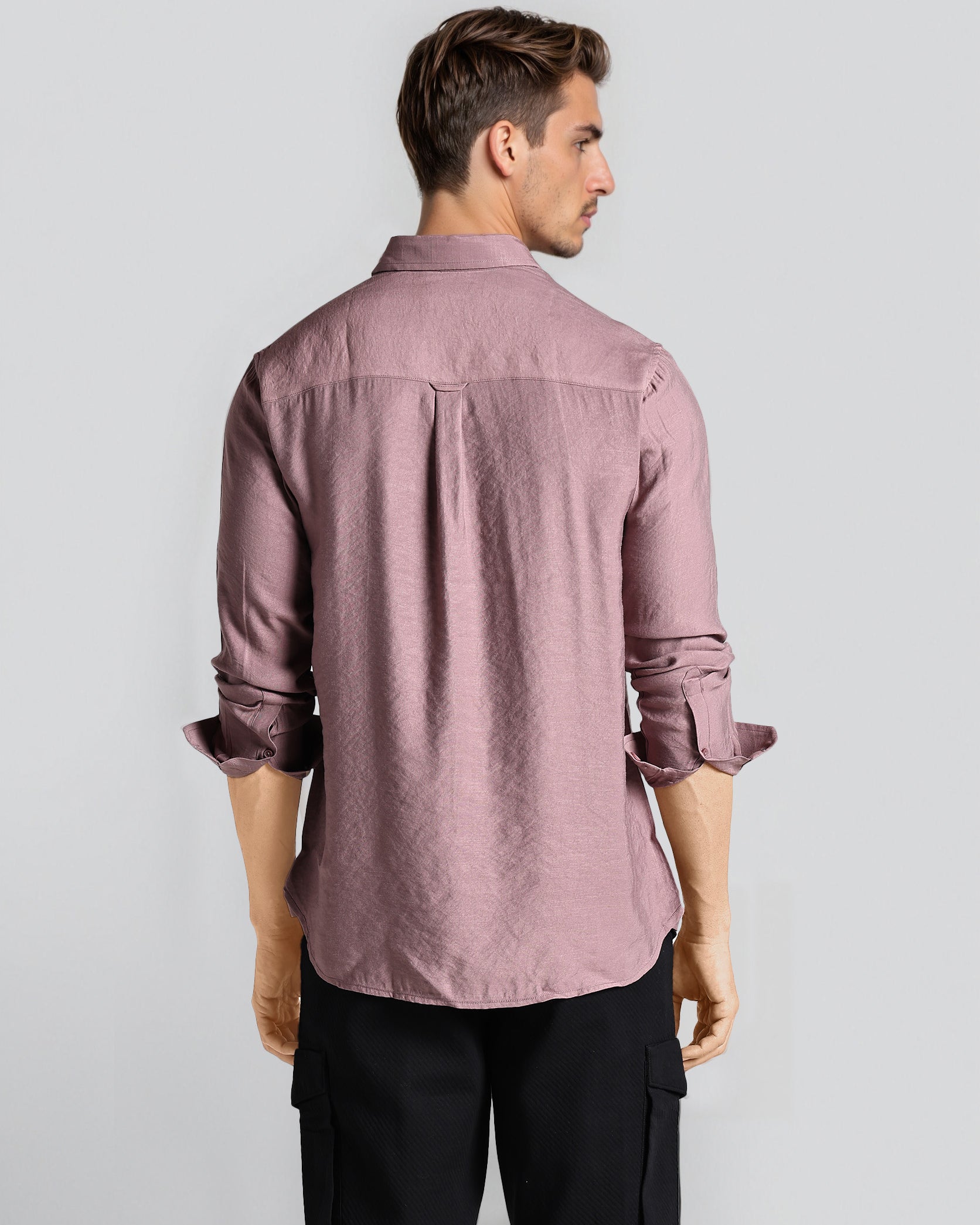 Man wearing a mauve button-up shirt and black pants on a light gray background