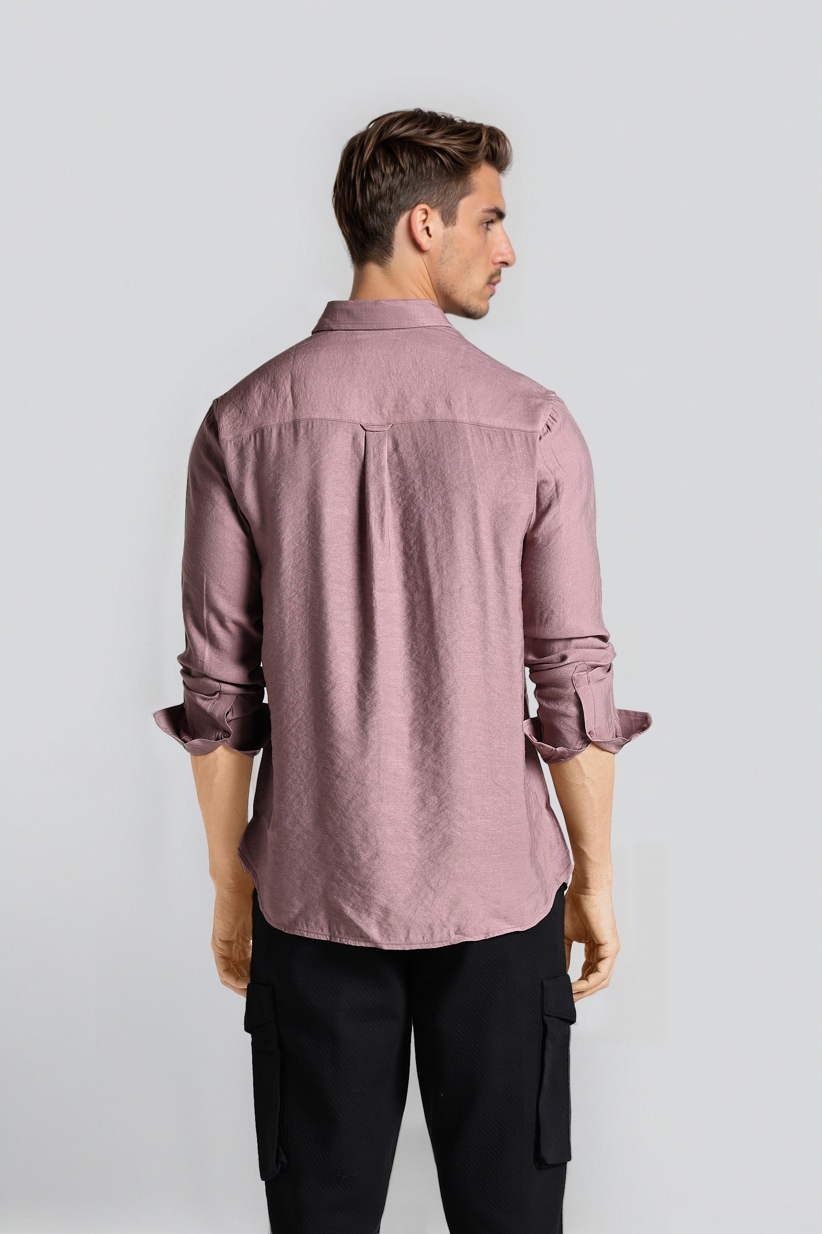 Man wearing a mauve button-up shirt and black pants on a light gray background