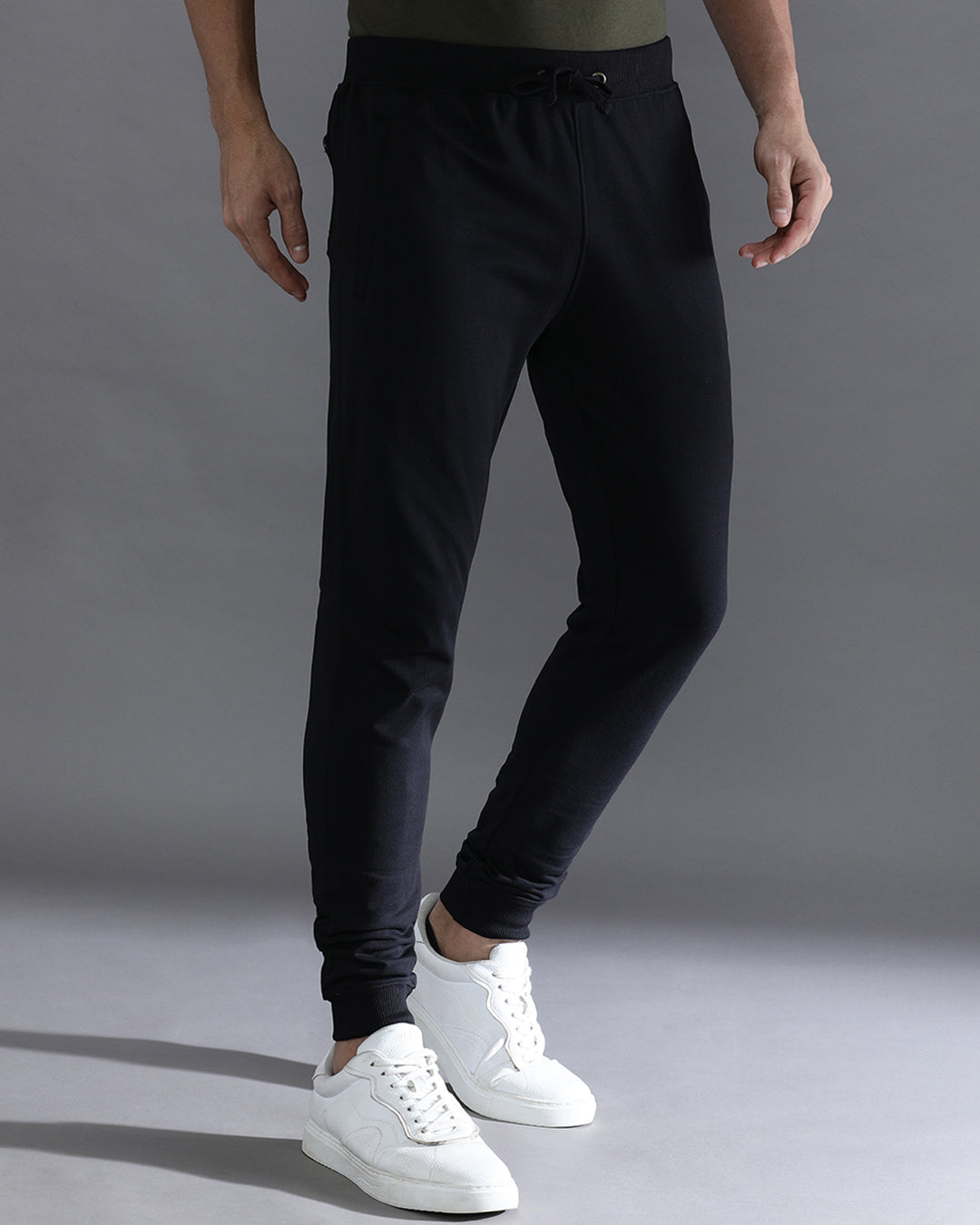 Person wearing black jogger pants and white sneakers on a gray background