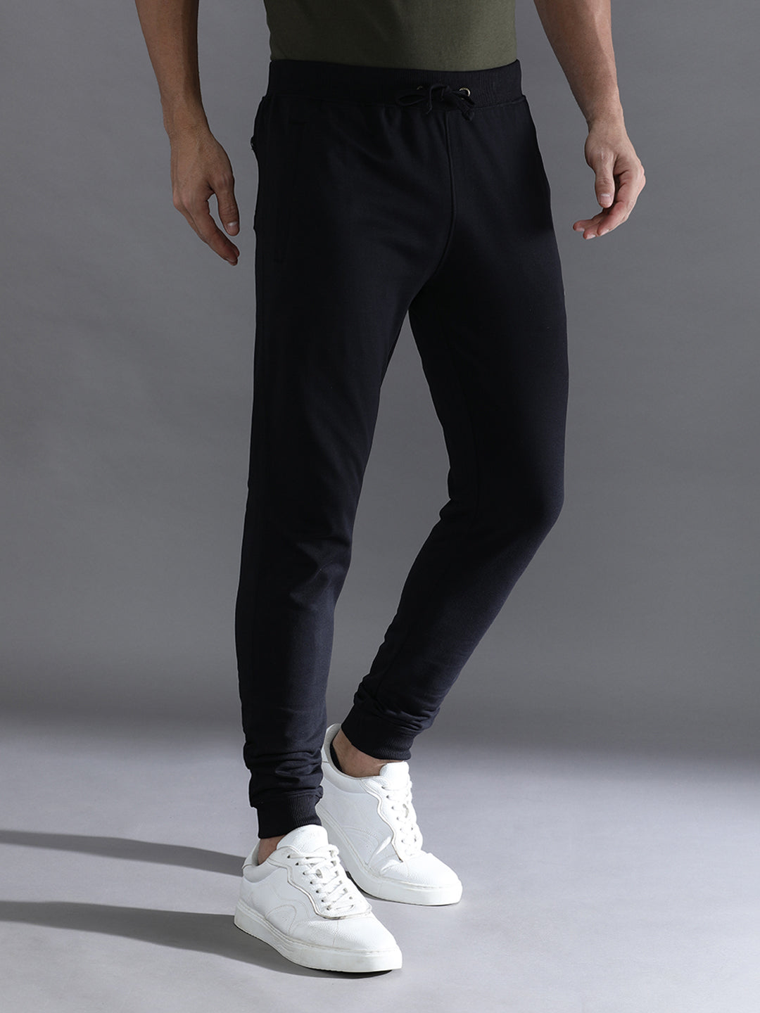 Person wearing black jogger pants and white sneakers on a gray background