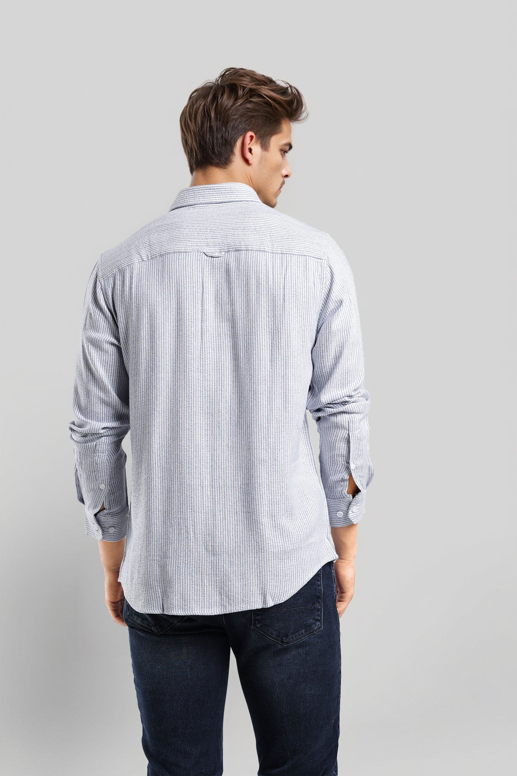 Man wearing a light blue striped shirt and dark pants on a gray background