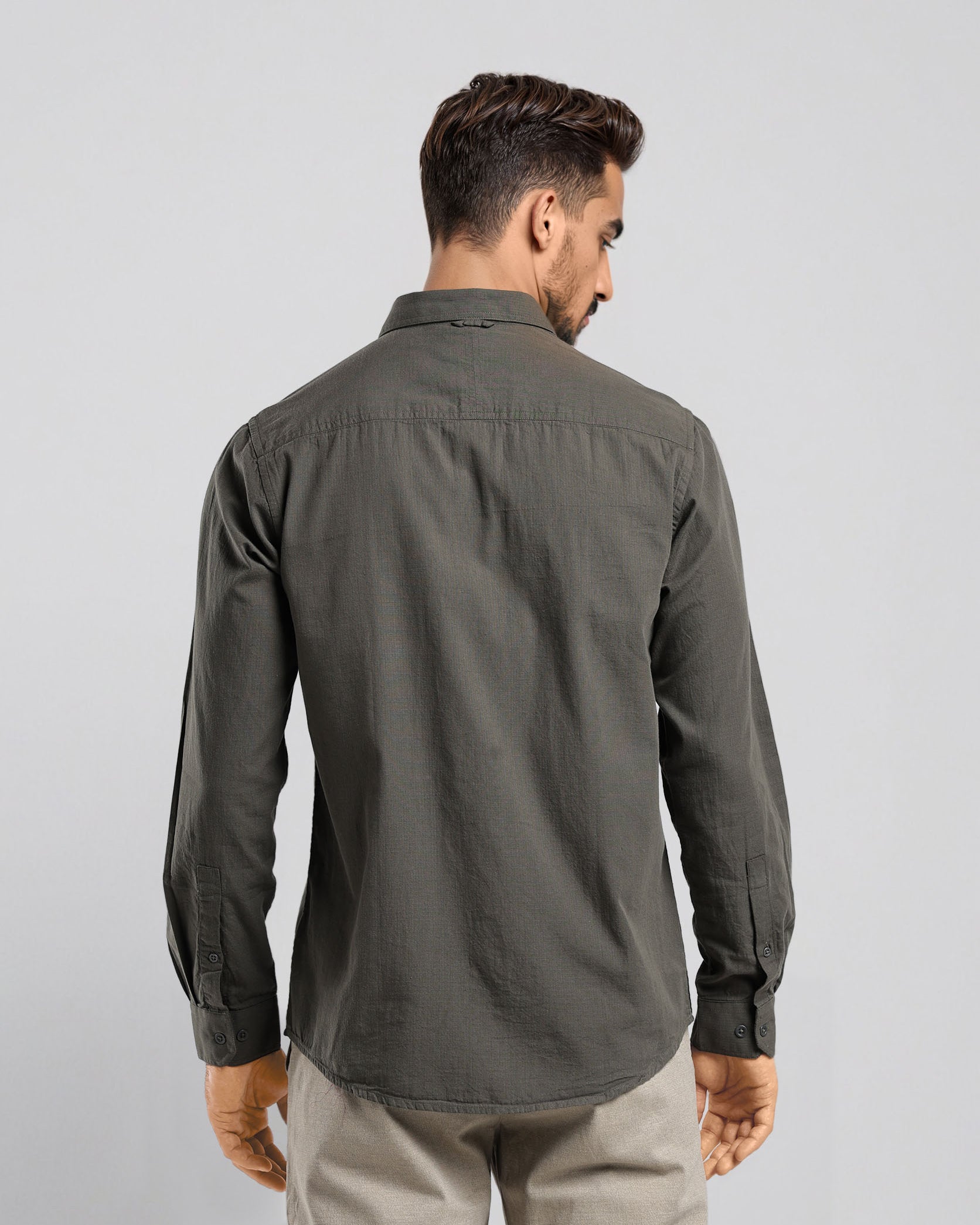 Man wearing a dark green shirt and beige pants on a light gray background