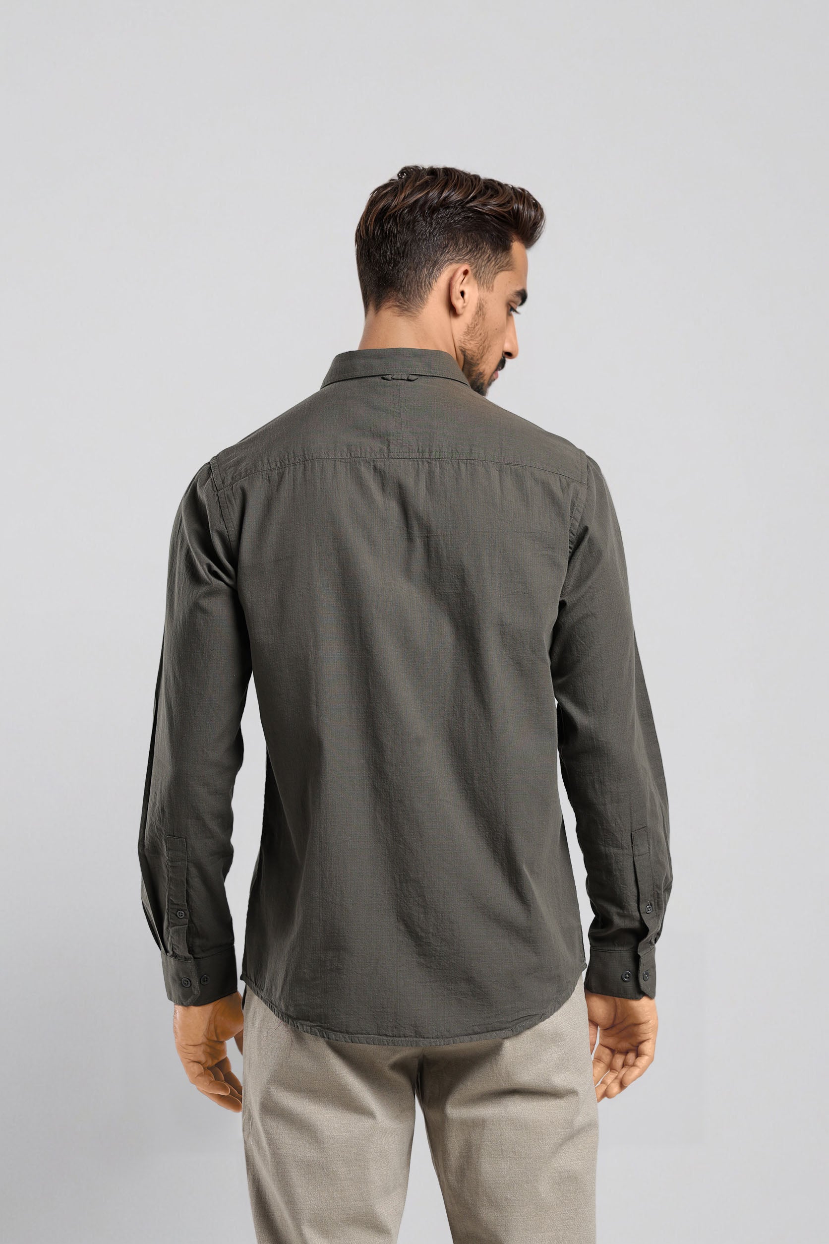 Man wearing a dark green shirt and beige pants on a light gray background